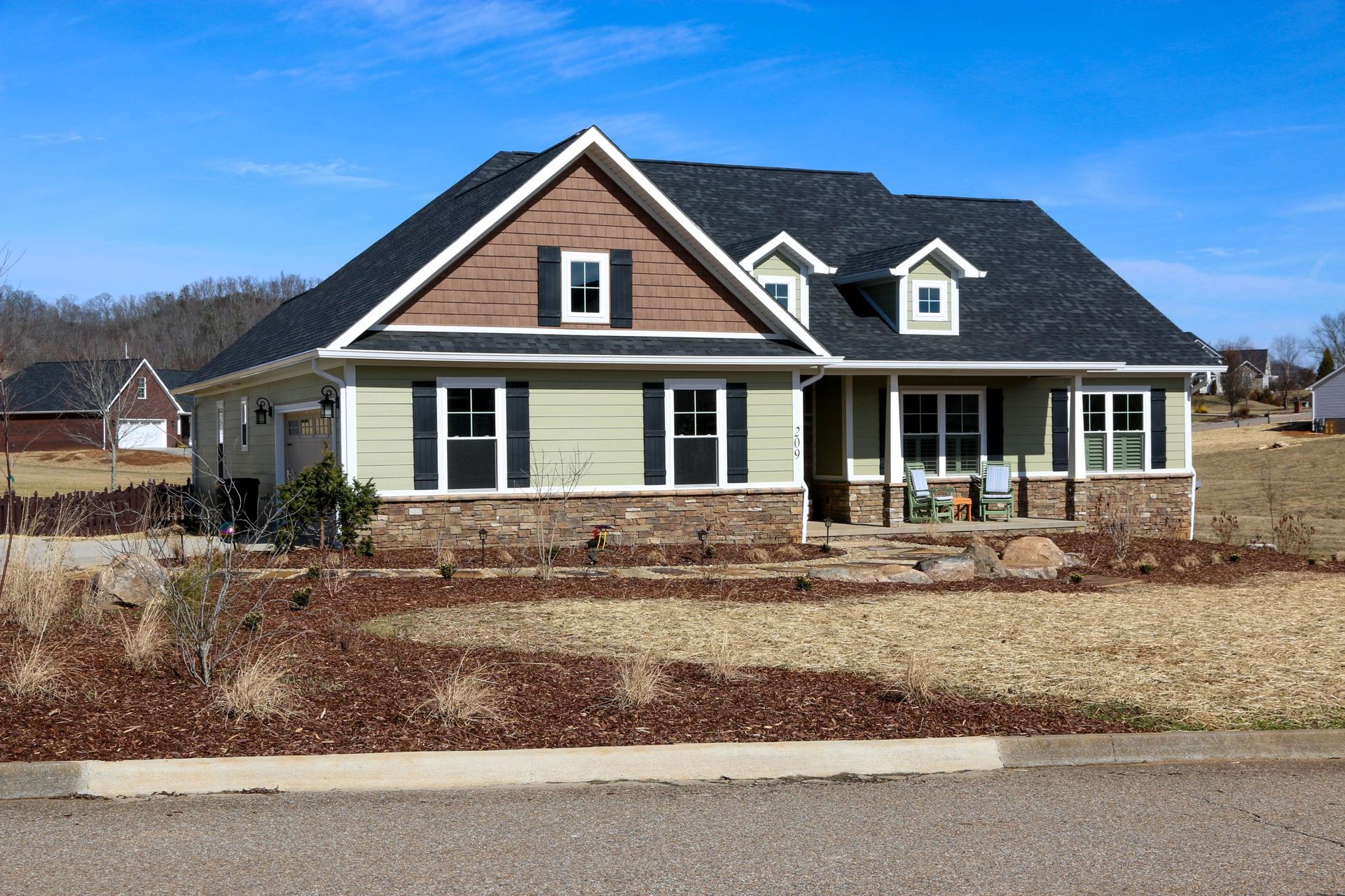 New suburban house with tan siding, brown roof, and a front porch under a clear blue sky