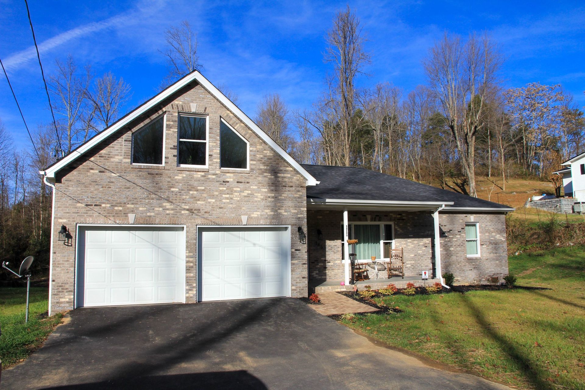 Suburban two-story house with stone facade, double garage, and front porch in a sunny yard