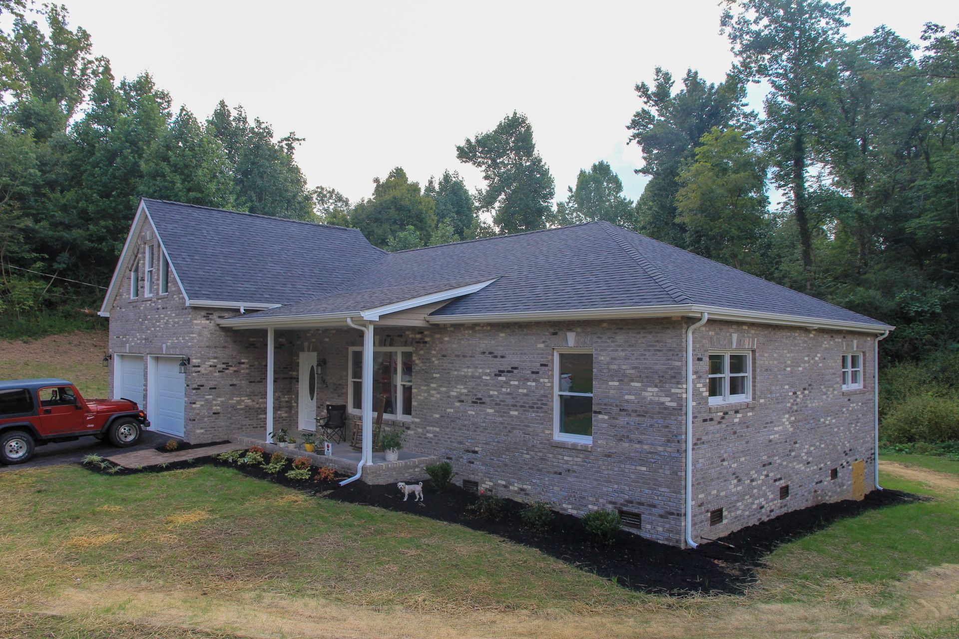 Single-story brick house with a gray roof, white trim, and a front porch in a grassy yard.