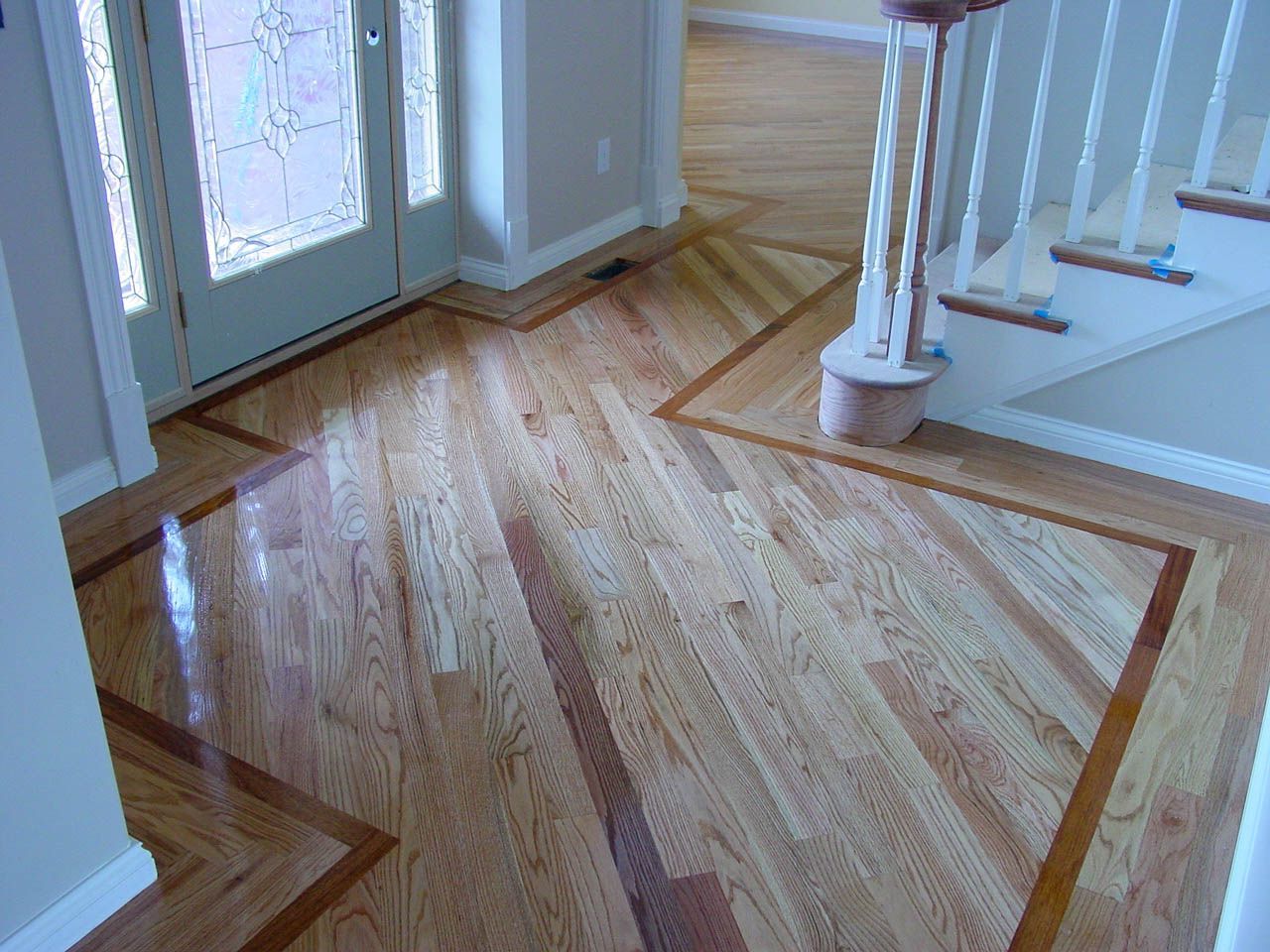 Wooden hardwood floor in a bright entryway with stairs and a front door.