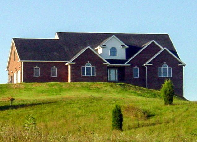Large red brick house on a grassy hill under a clear blue sky