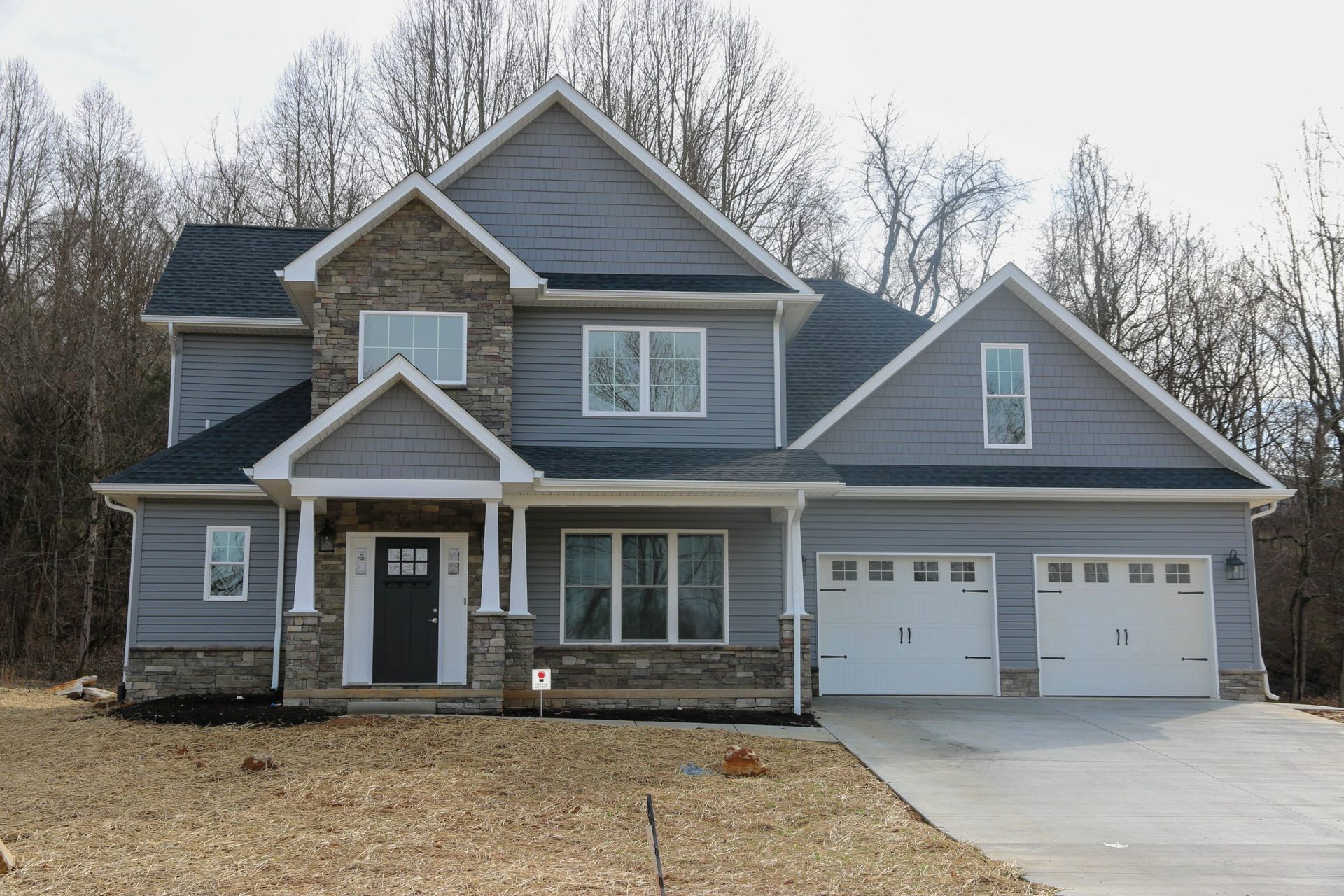 Two-story gray house with white trim, front porch, and double garage in a suburban neighborhood