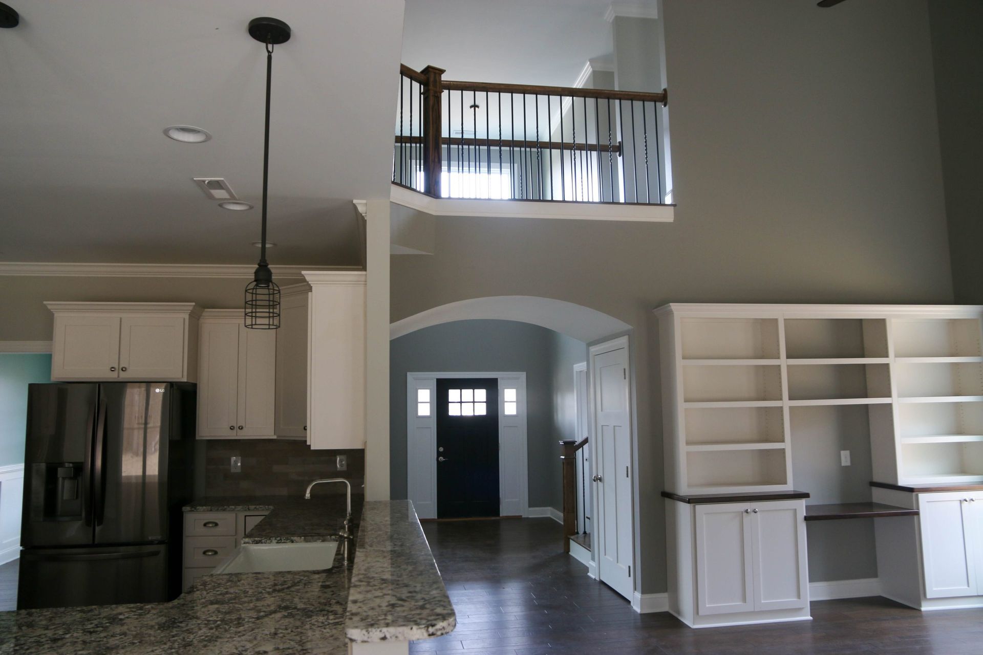 Open-concept kitchen and entryway with granite counters, white built-ins, and a lofted balcony.