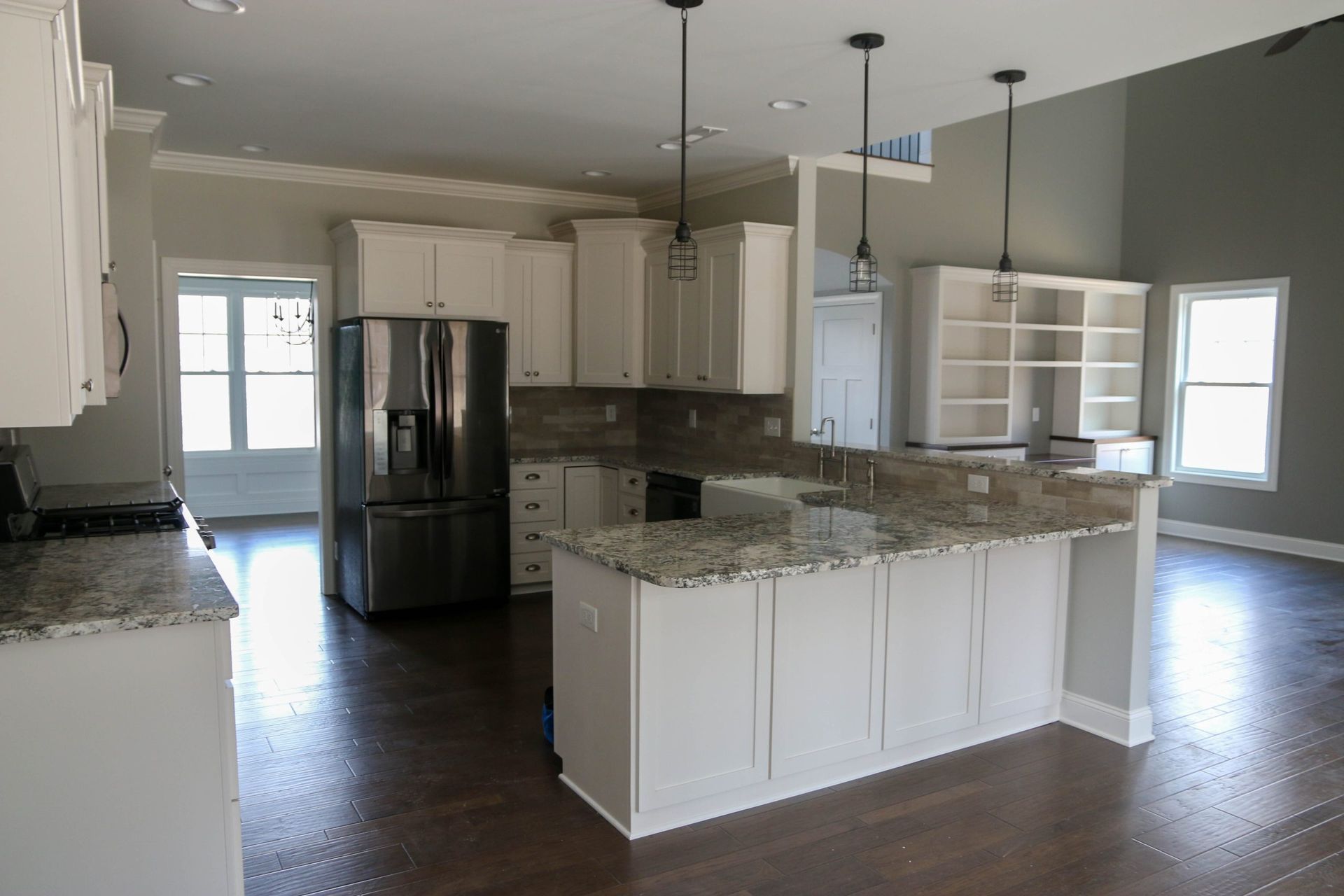 Modern kitchen with granite island, white cabinets, stainless steel fridge, and dark wood floors