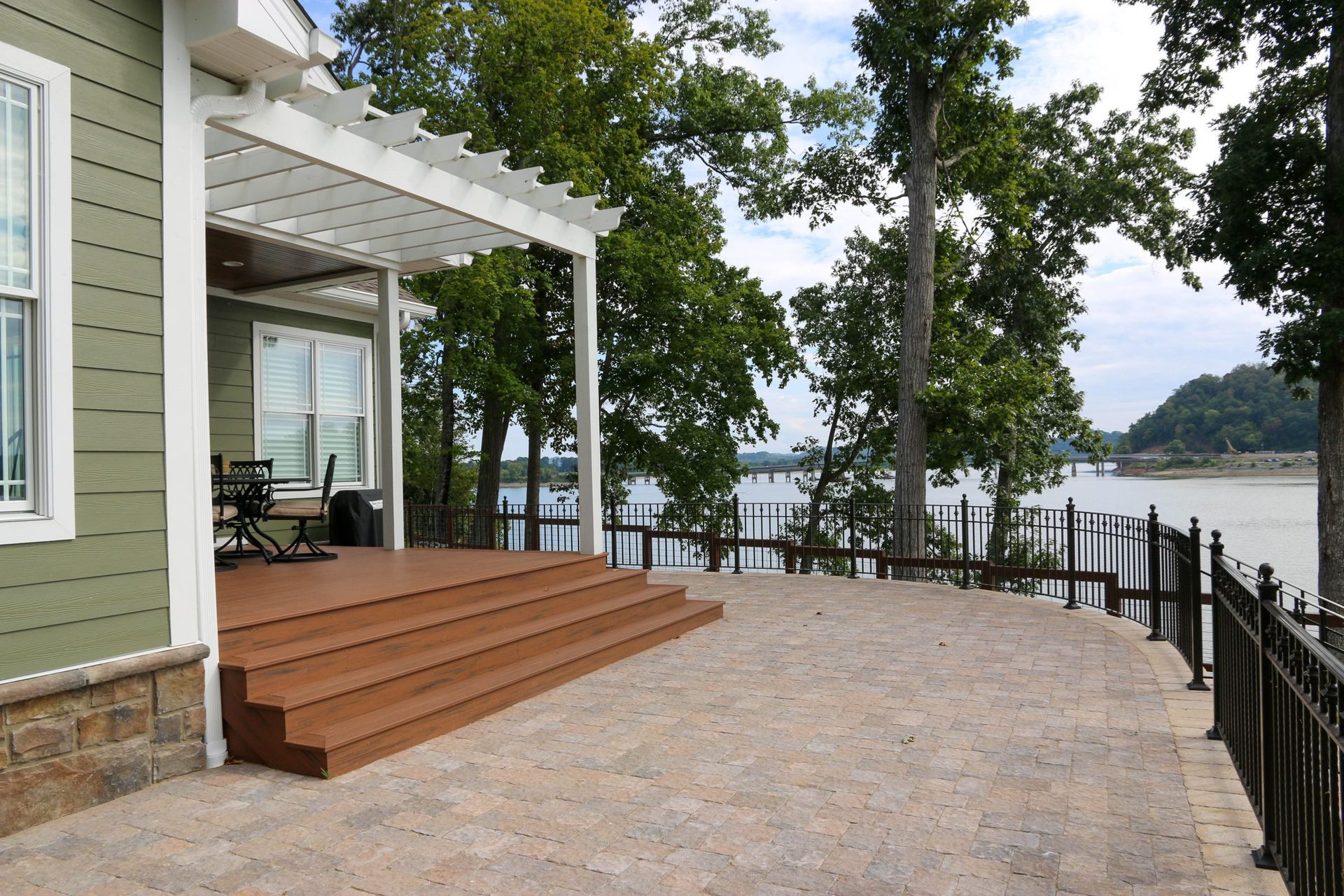 Patio with wooden steps, pergola, and river view beside a house