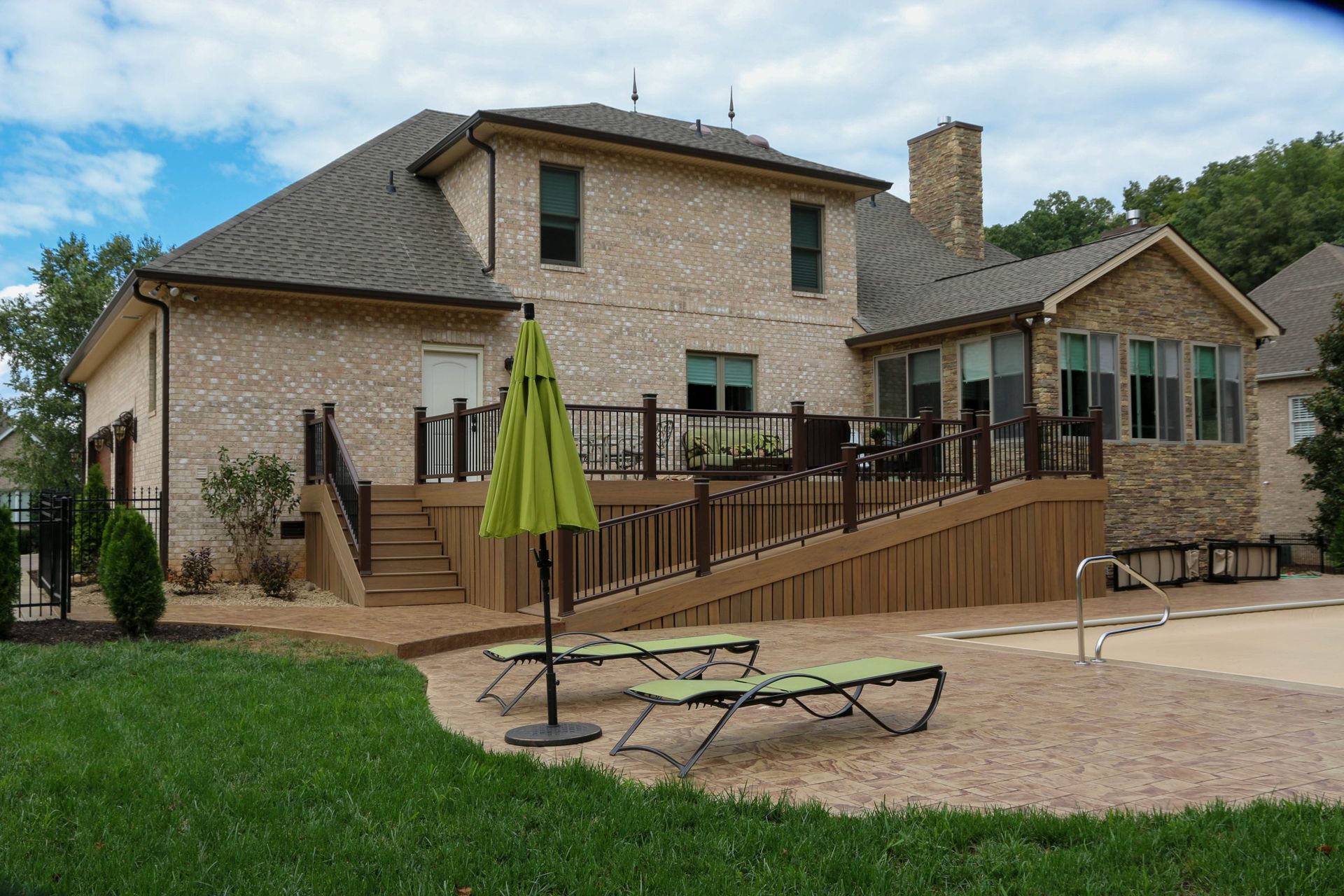 Stone house with wooden deck, patio chairs, and green umbrella in a grassy yard
