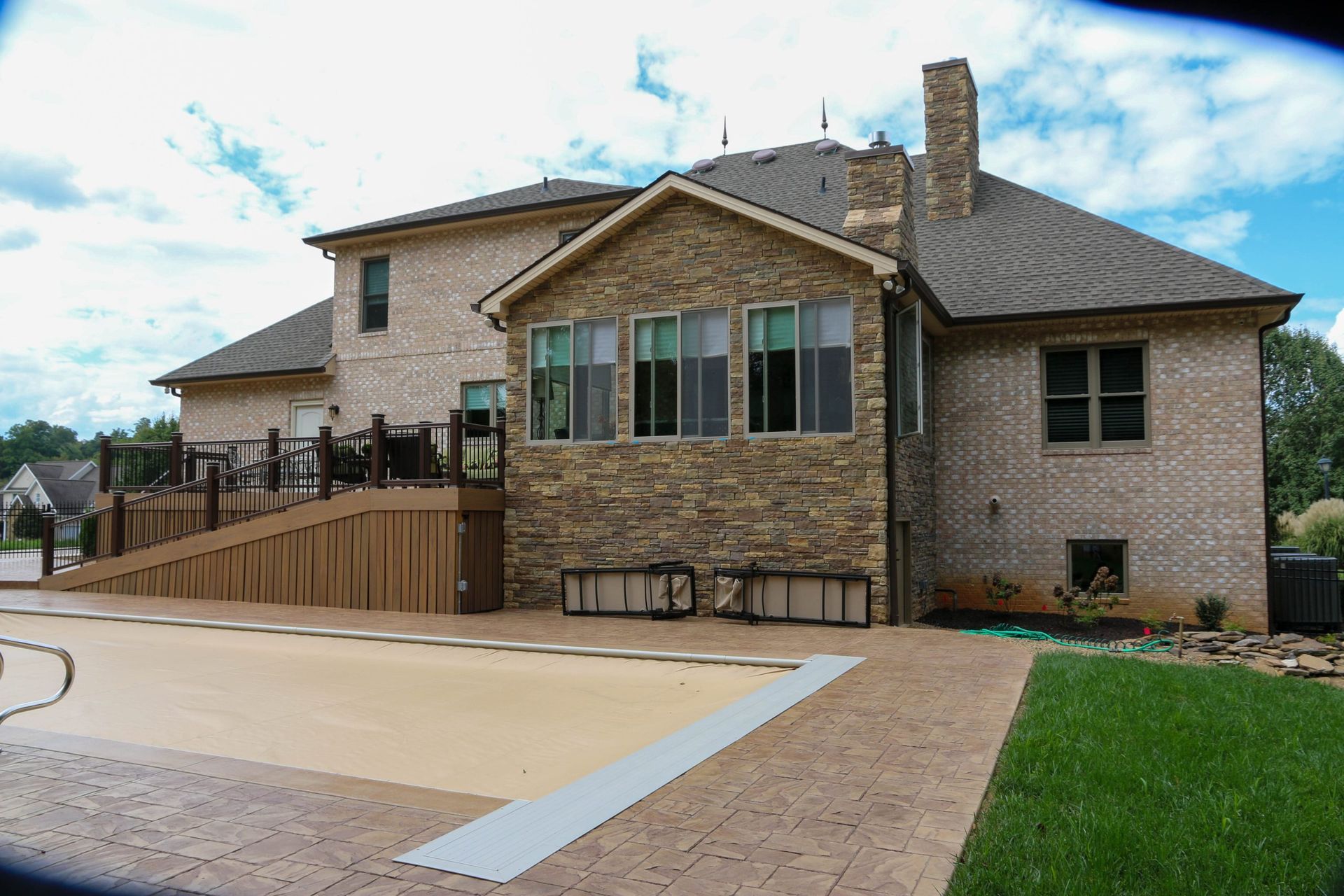 Brick house with a ramped deck and small patio beside a driveway and lawn