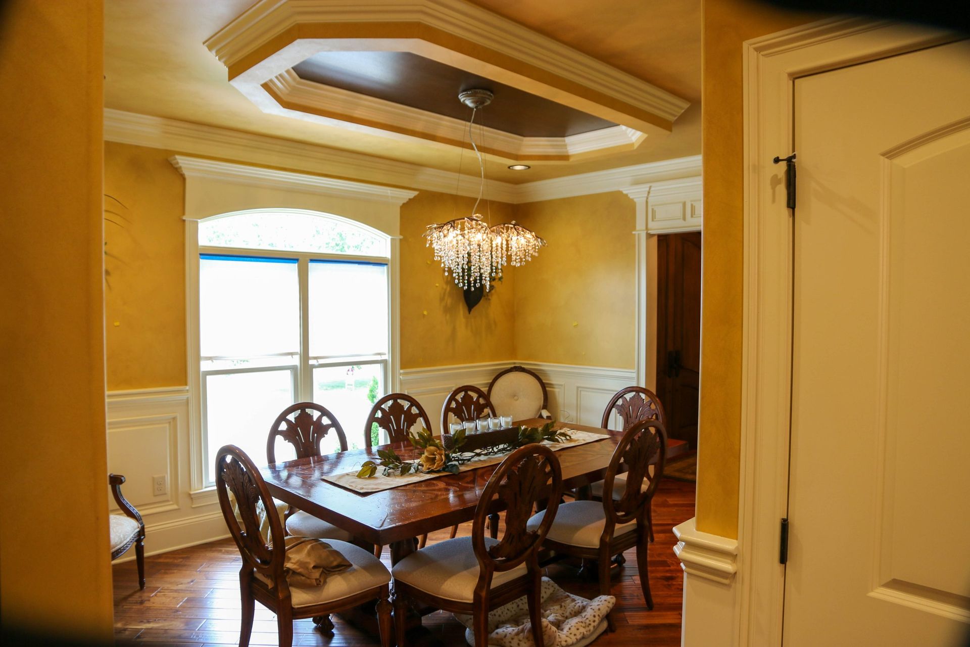 Elegant dining room with ornate chandelier, polished table, and cream walls beneath a coffered ceiling