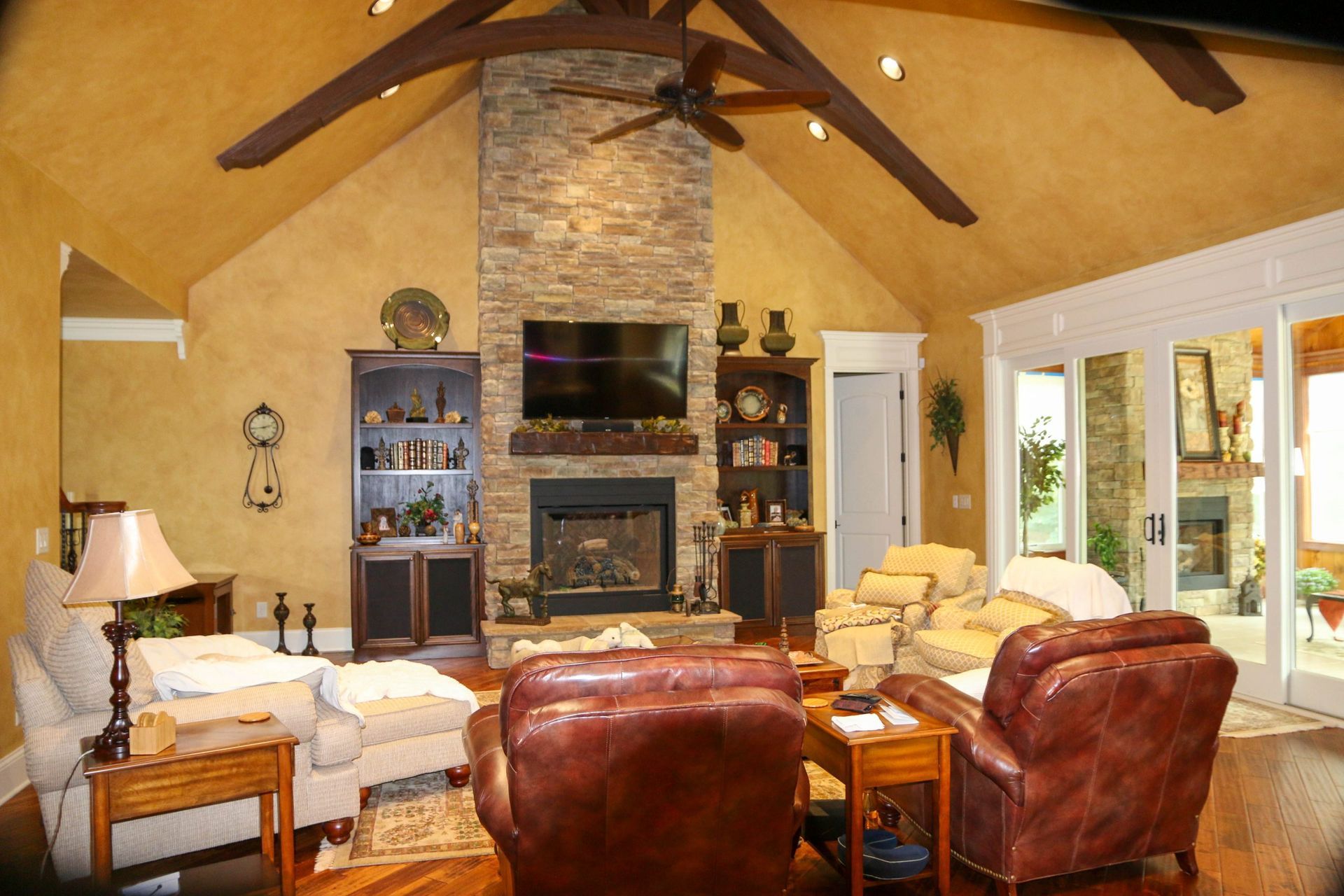 Cozy living room with high wood ceiling, stone fireplace, leather chairs, and large windows