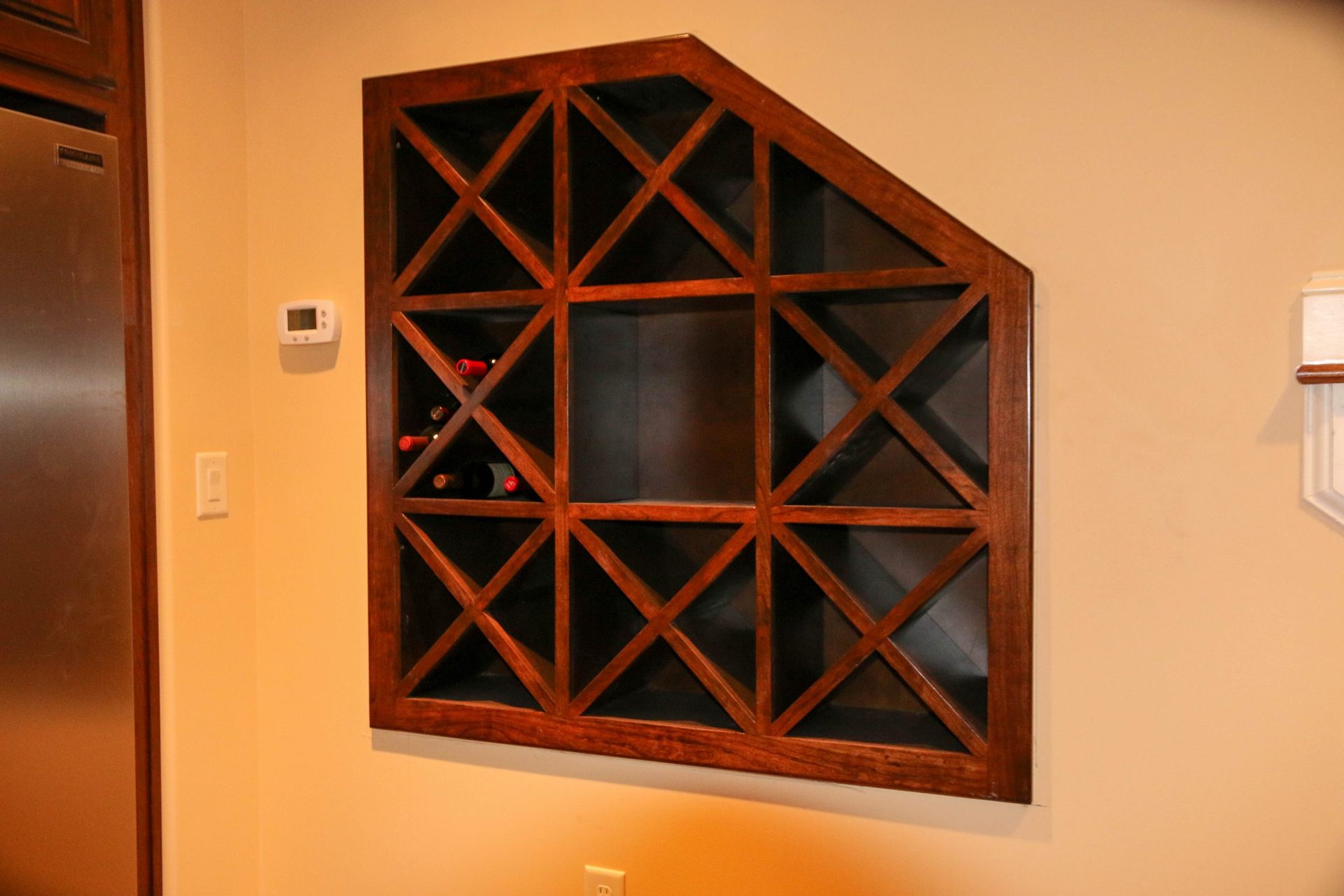 Wall-mounted wooden wine rack with diamond-shaped cubbies on a beige interior wall.
