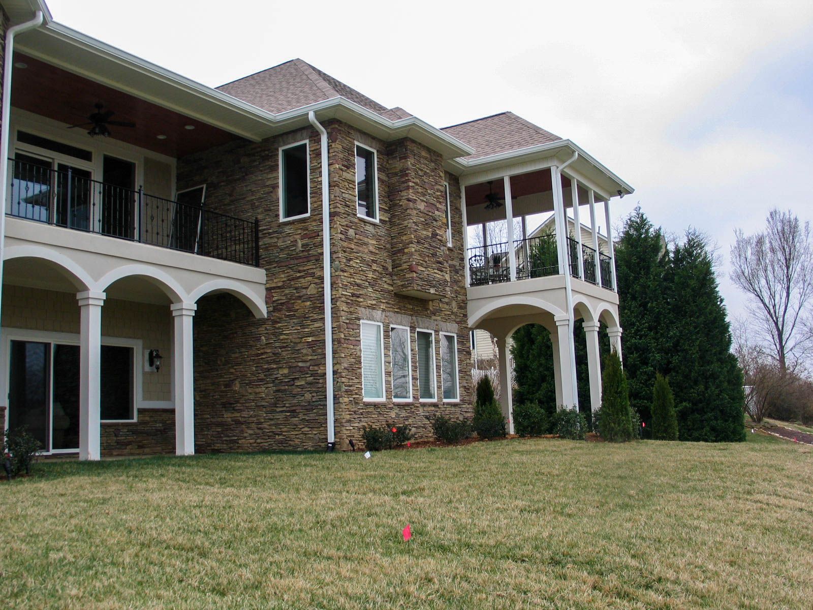 Large brick house with white arches and balconies on a grassy lawn under an overcast sky