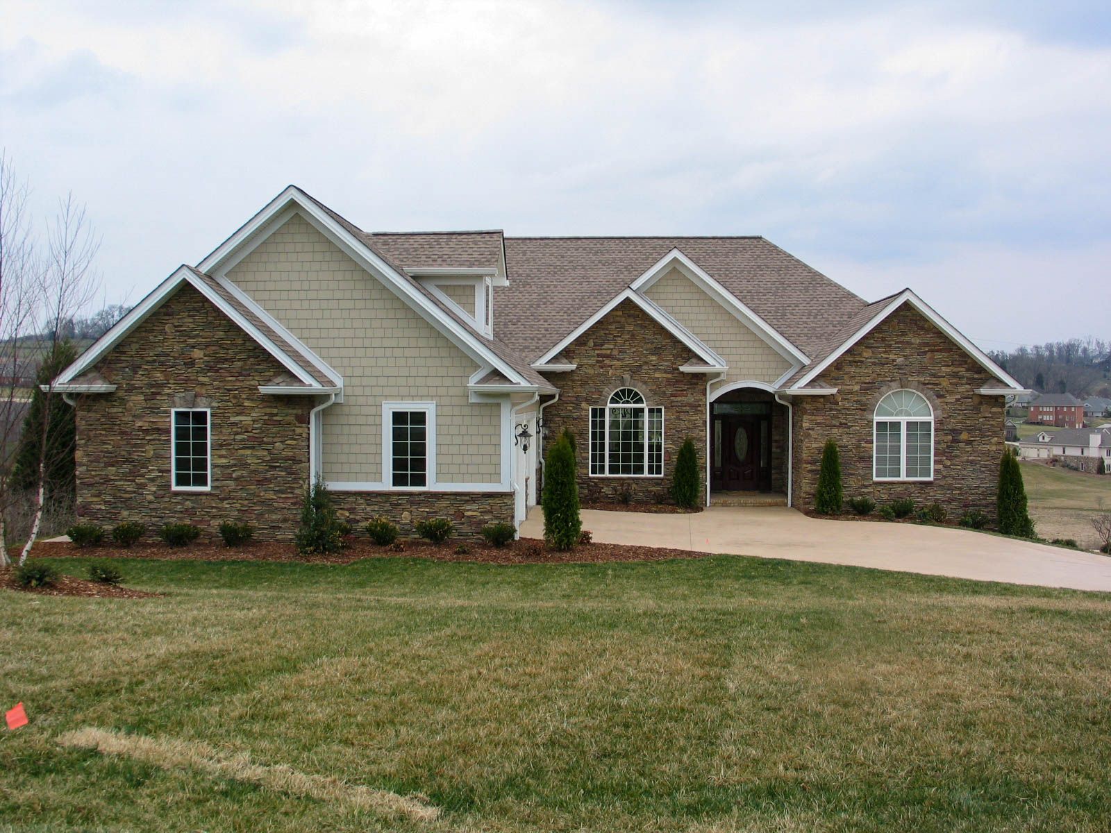 Large suburban brick house with beige siding and a two-car garage, viewed from a grassy front yard