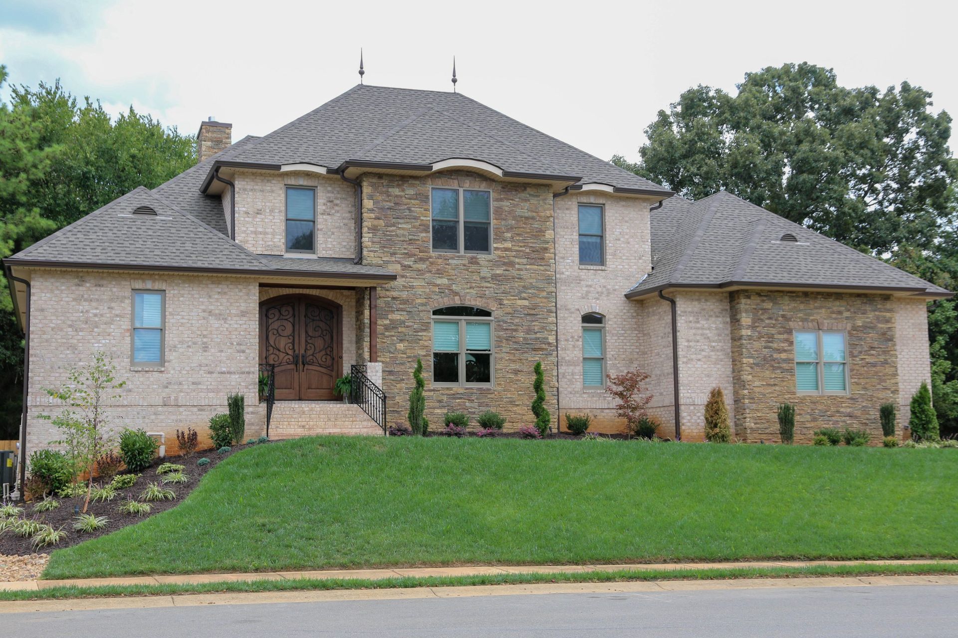 Large two-story brick house with gray roof and green lawn in a suburban neighborhood