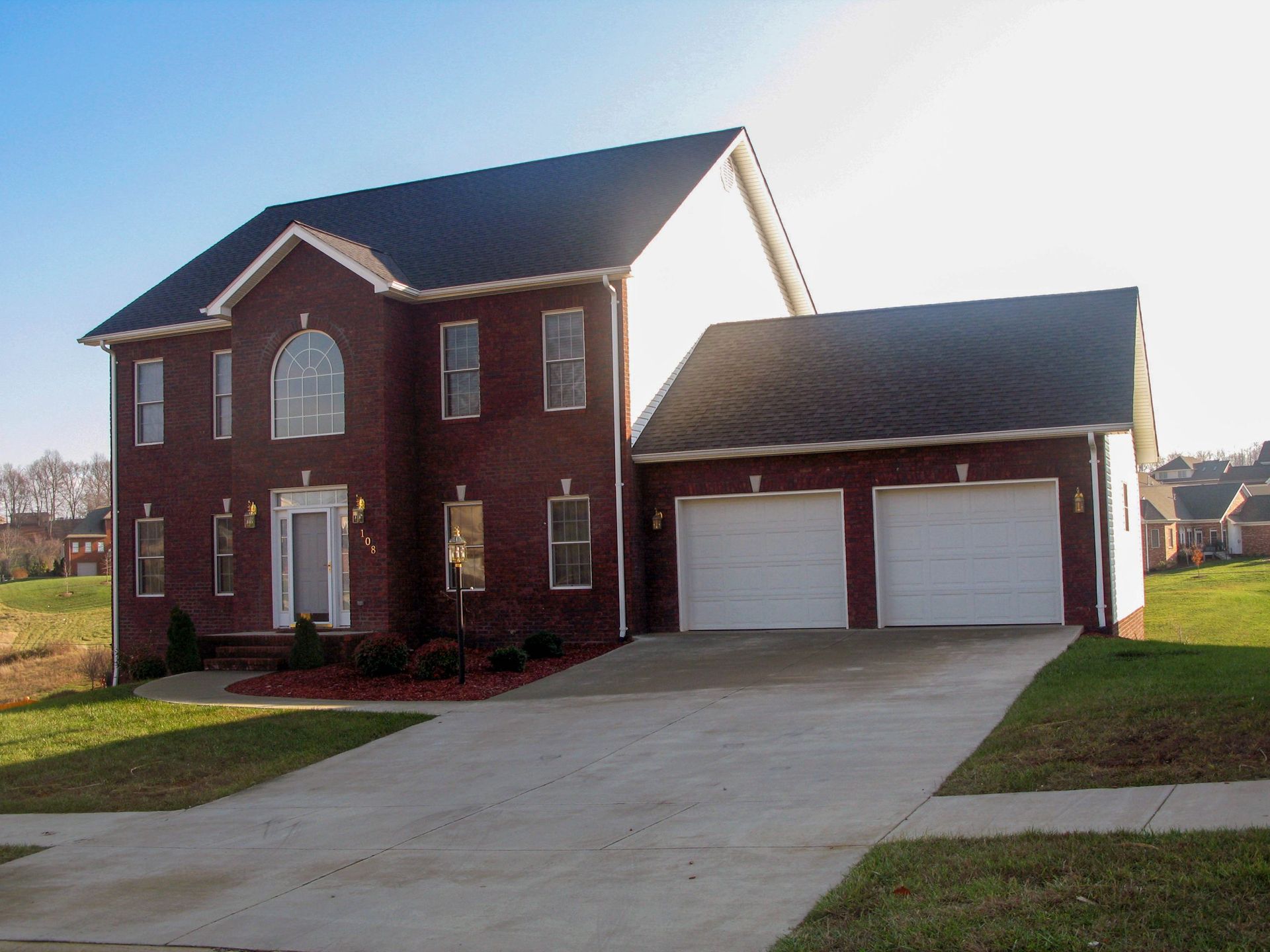 Two-story brick house with a two-car garage and driveway on a sunny day