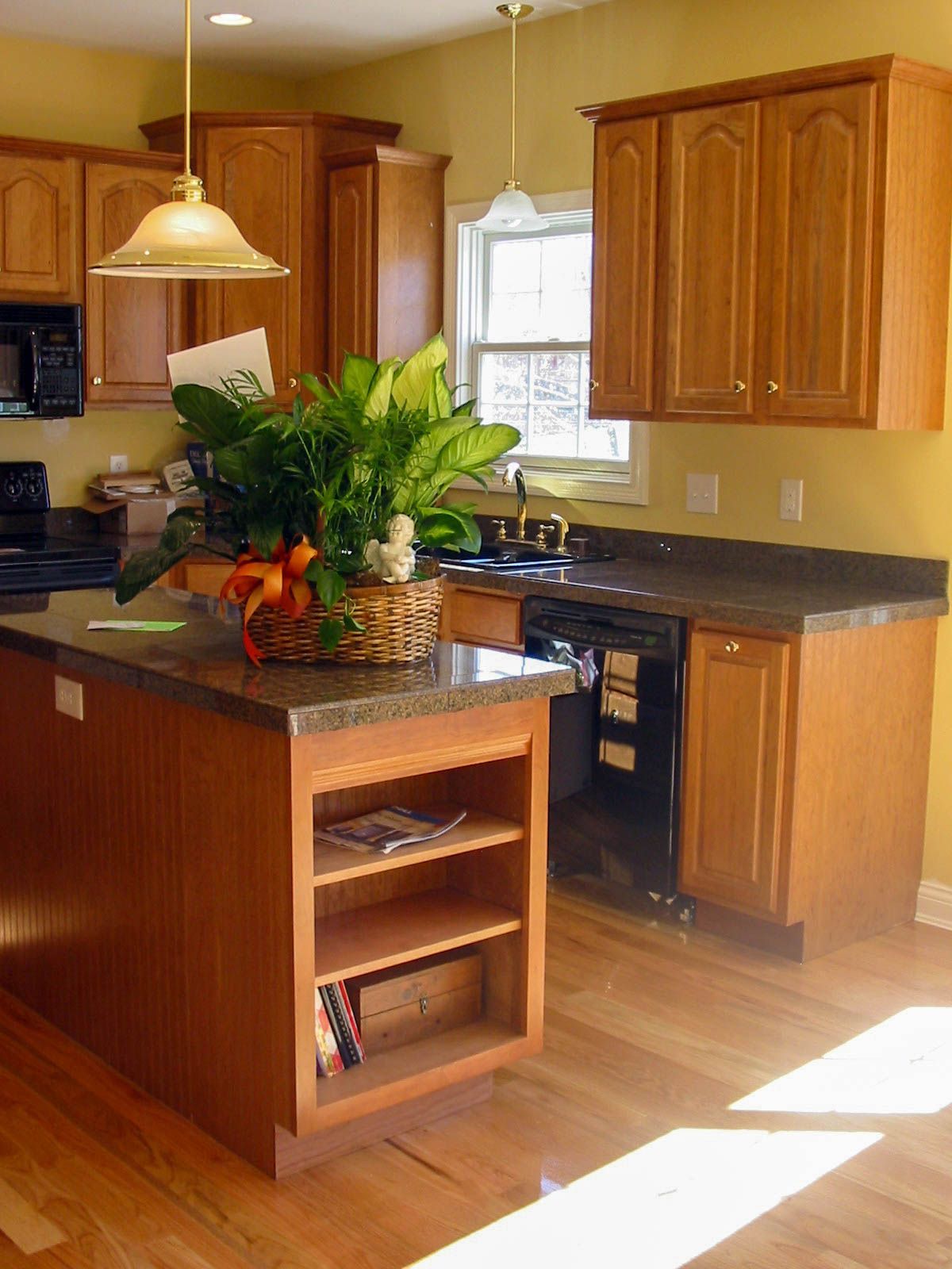 Kitchen with wood cabinets, dark countertops, island, pendant light, and a plant centerpiece in warm sunlight