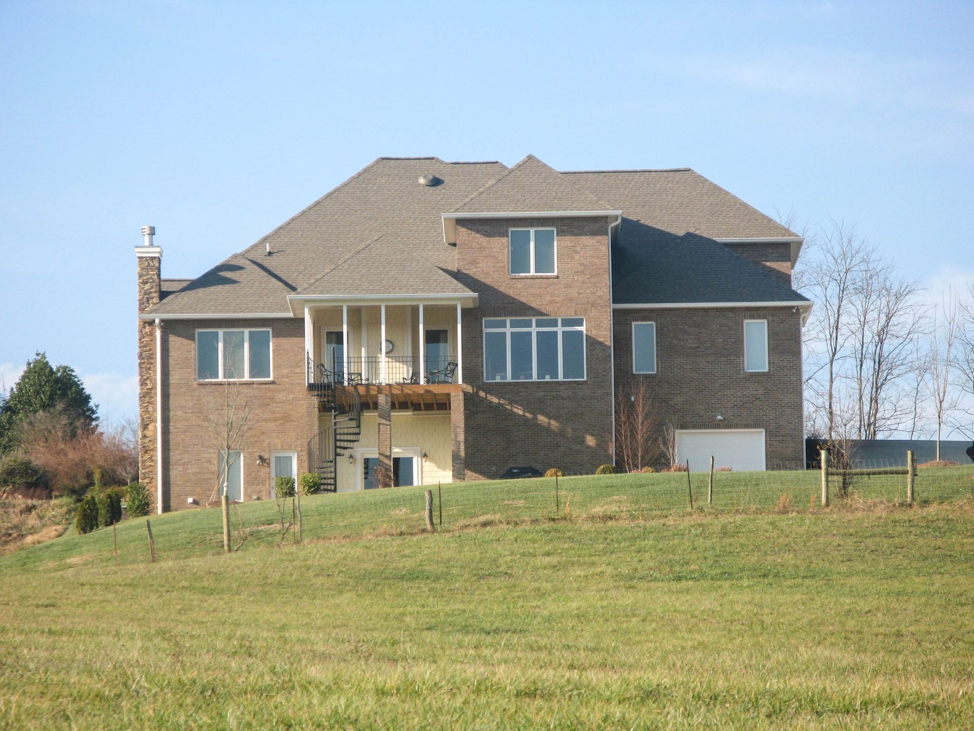 Large brick house with a tan roof on a grassy hill under a clear blue sky