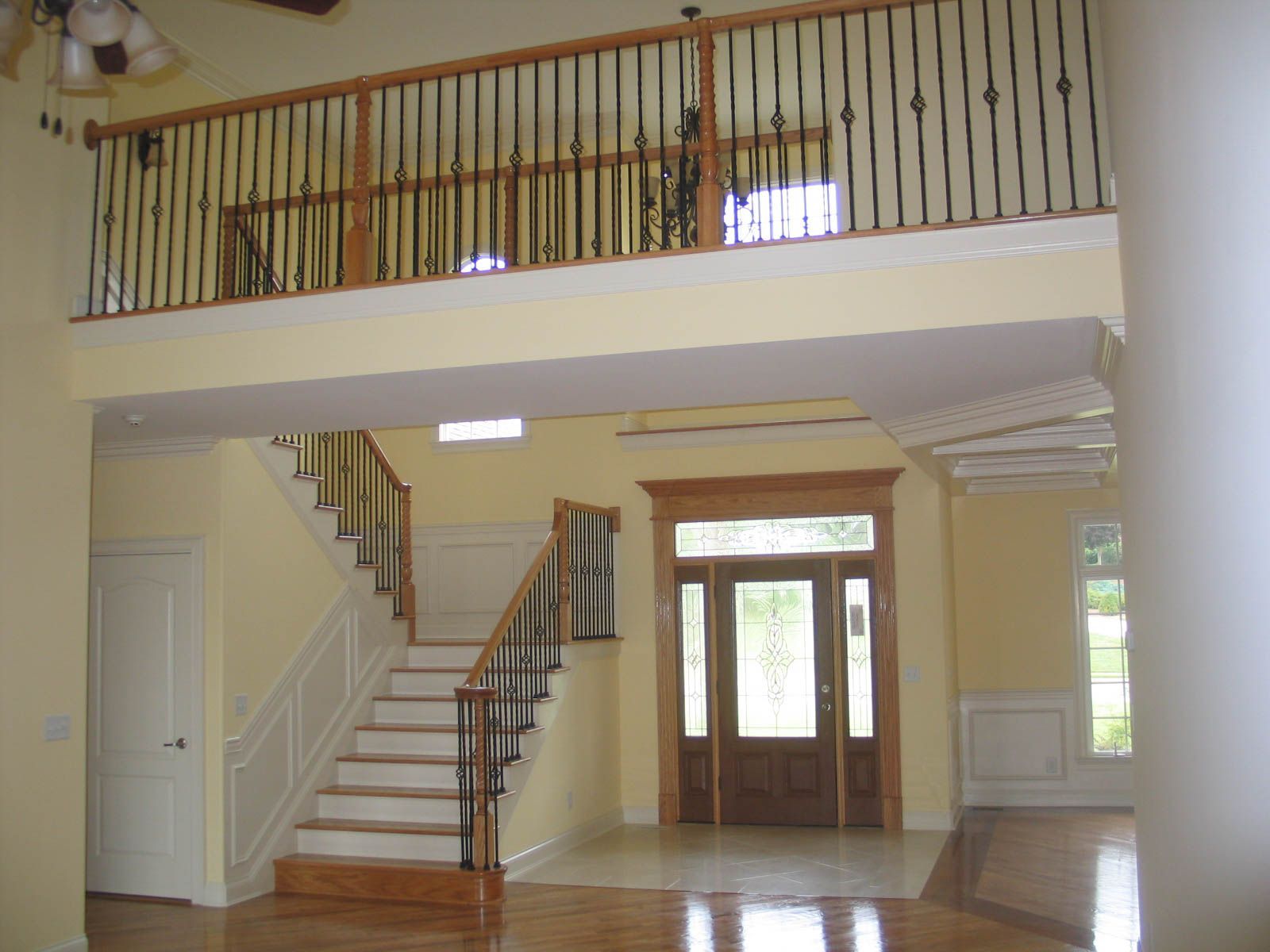 Spacious foyer with staircase, balcony railing, and front double doors in a bright home interior
