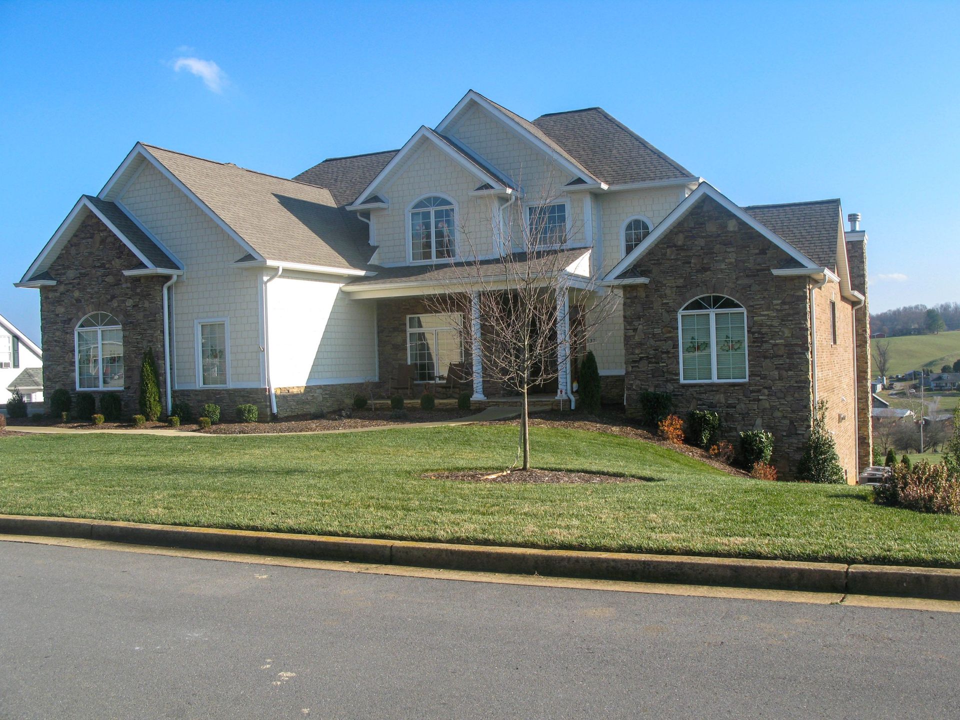 Large suburban house with stone and white siding, a front lawn, and a driveway under a clear blue sky