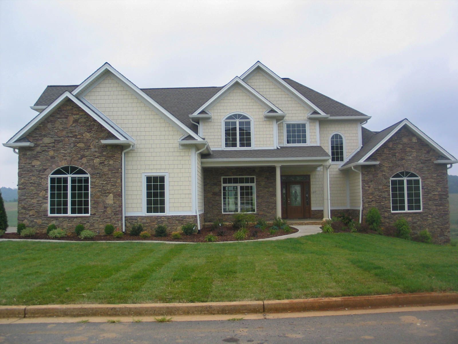 Large suburban house with beige siding, brick accents, and a manicured green lawn