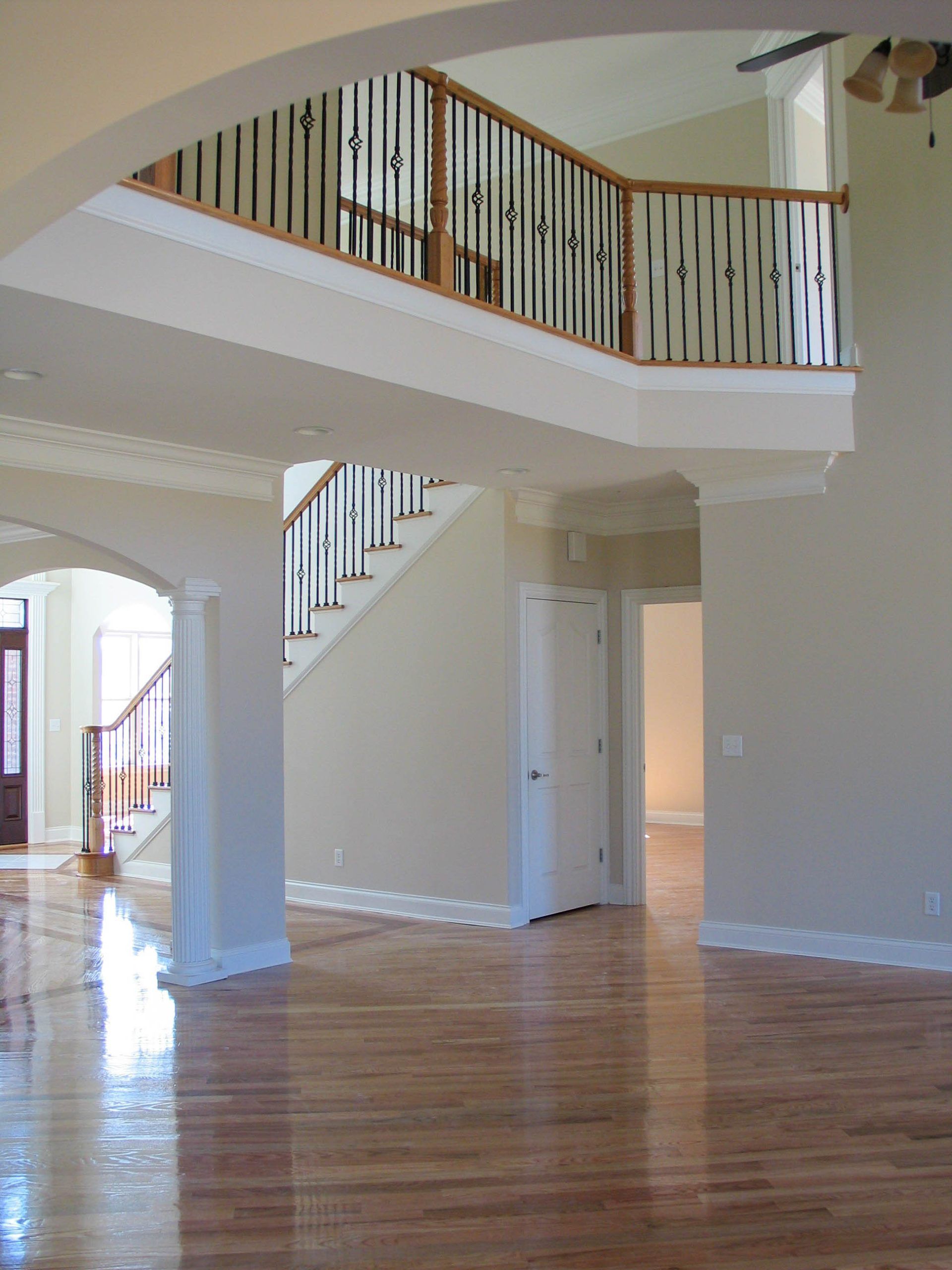 Spacious empty living room with hardwood floors, staircase, and white walls featuring an open upstairs balcony.