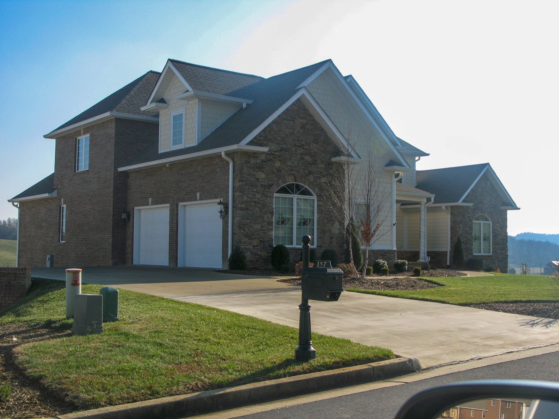 Suburban brick house with two-car garage, front lawn, and driveway on a sunny day