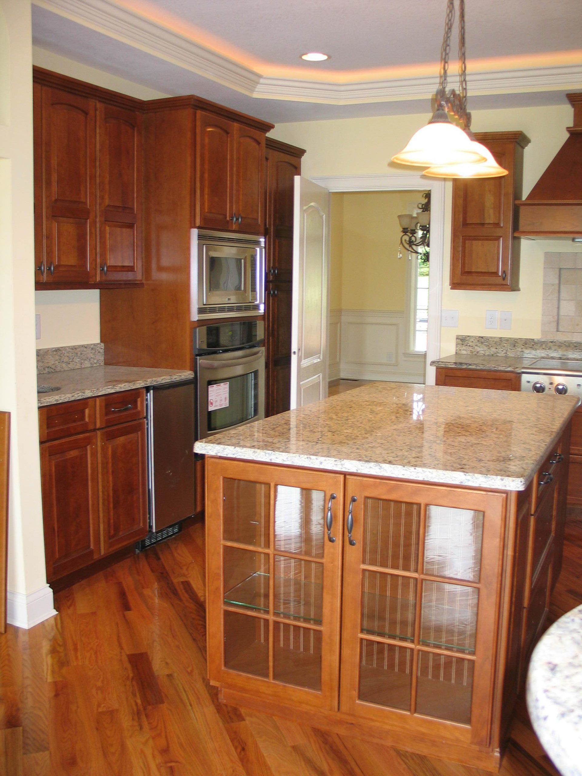 Warm kitchen with wood cabinets, granite island, built-in ovens, and hanging pendant light.