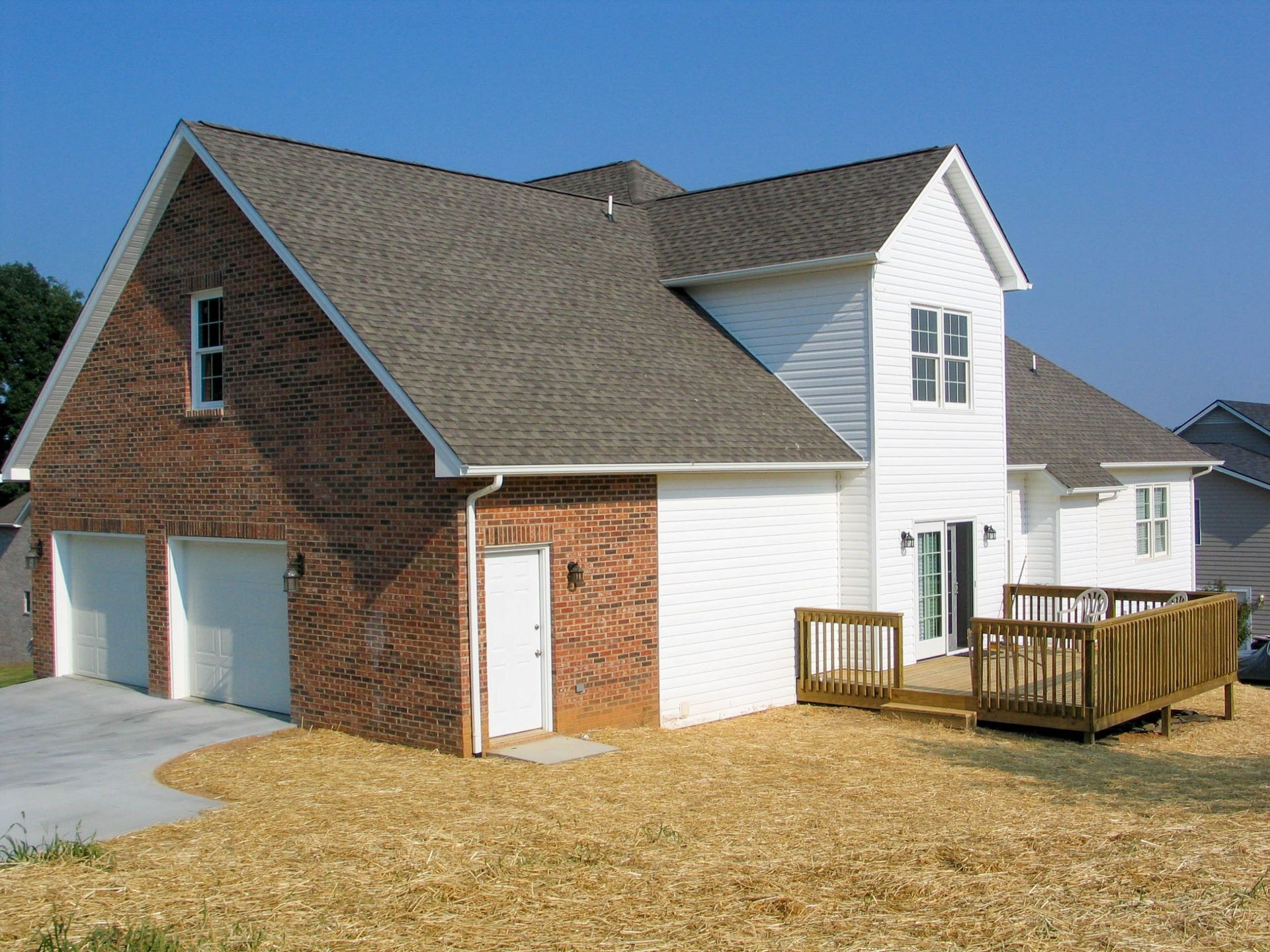 Suburban house with brick and white siding, attached garage, and wooden deck on a dry lawn