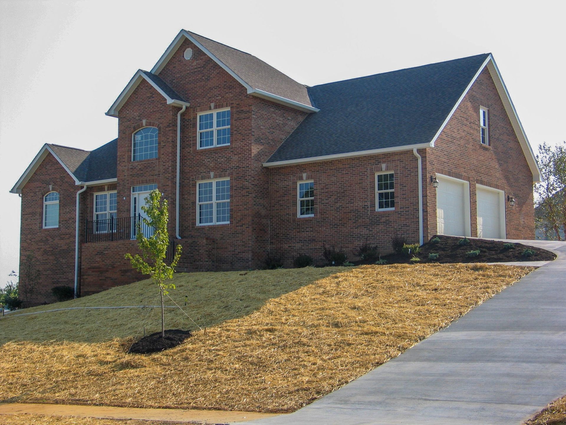 Brick house with a double garage and sloped driveway on a sunny day