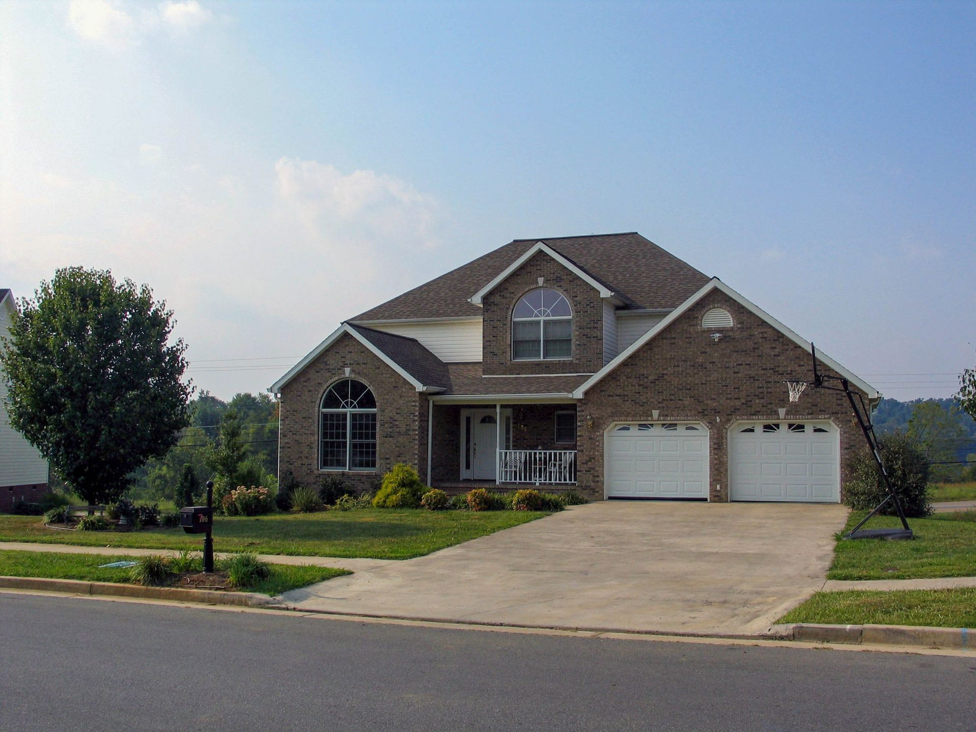 Brick suburban house with two-car garage, driveway, and front lawn under a clear sky