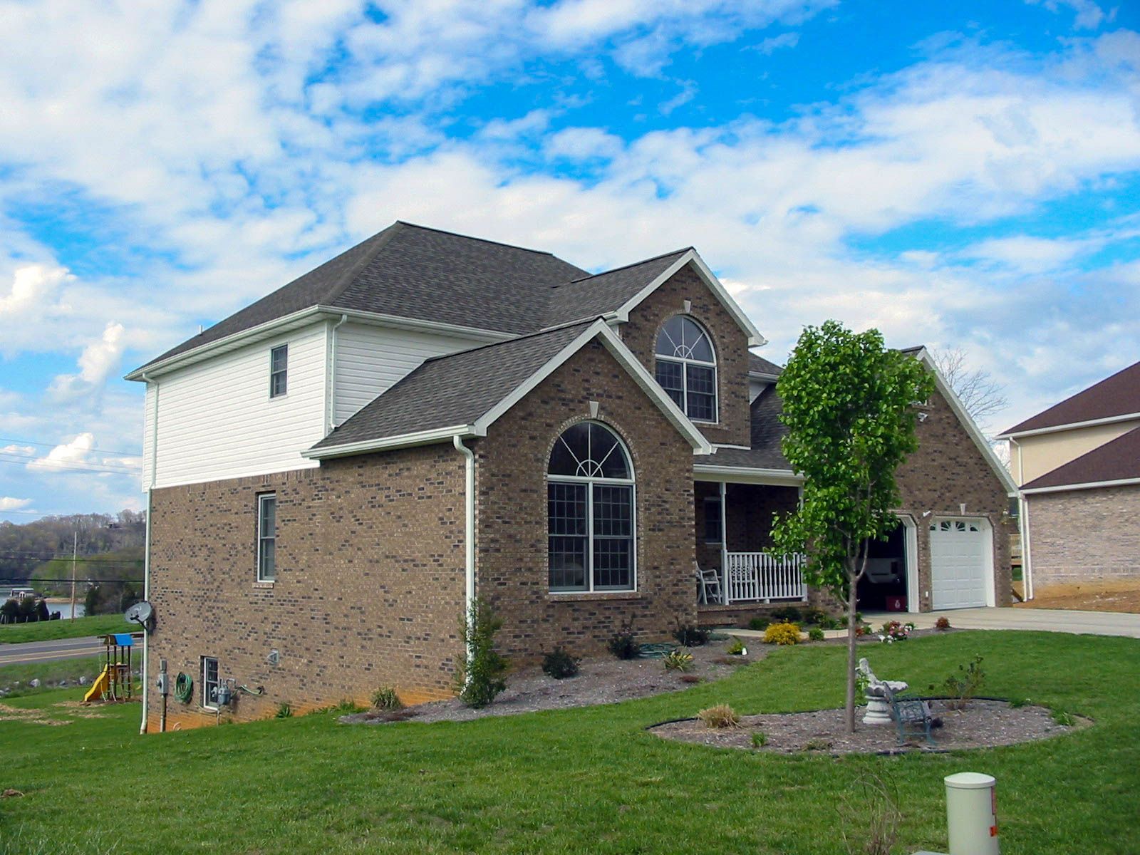 Two-story brick house with arched windows, a small front lawn, and a detached garage under a cloudy sky