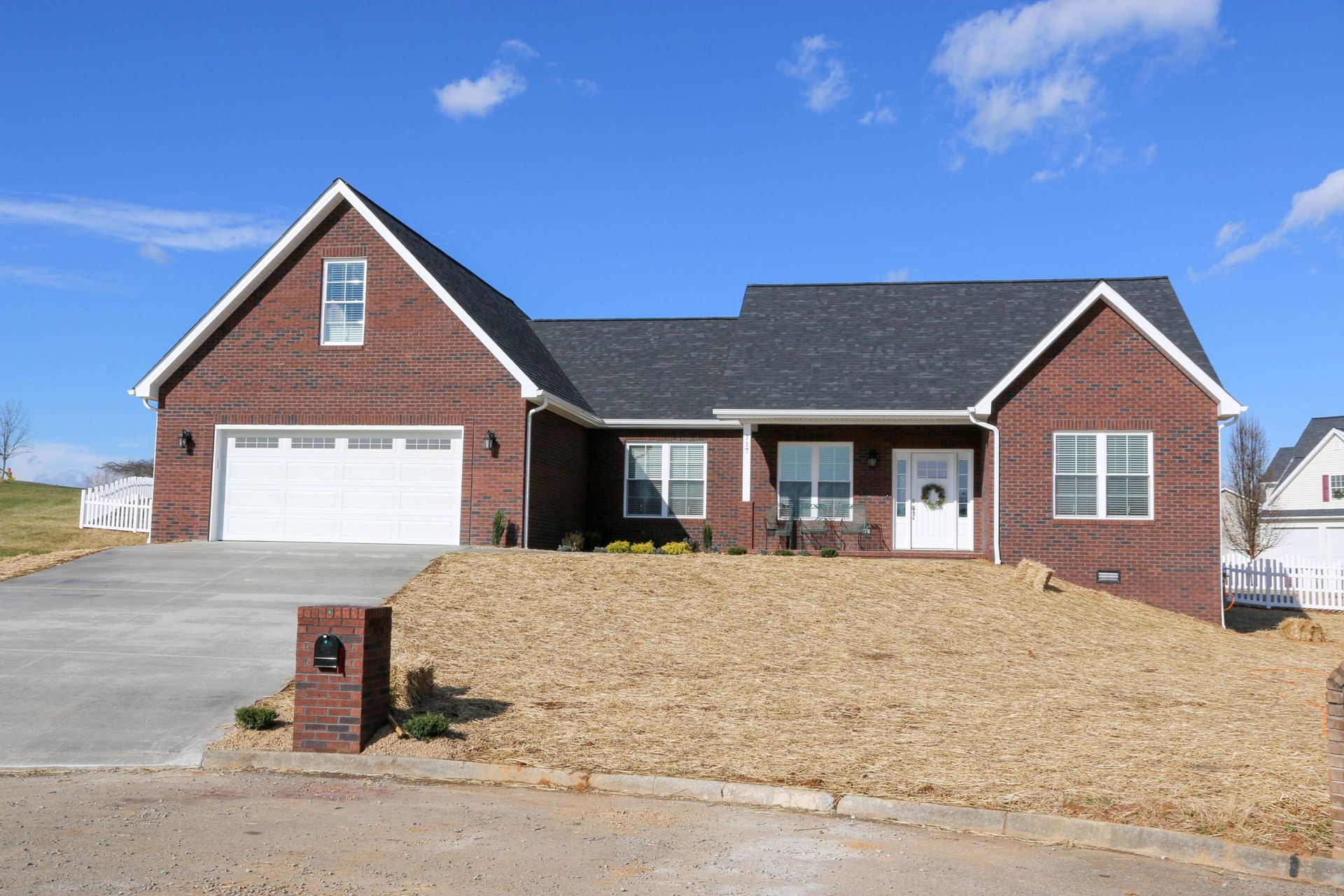 Brick house with white garage door and dry front yard under a blue sky