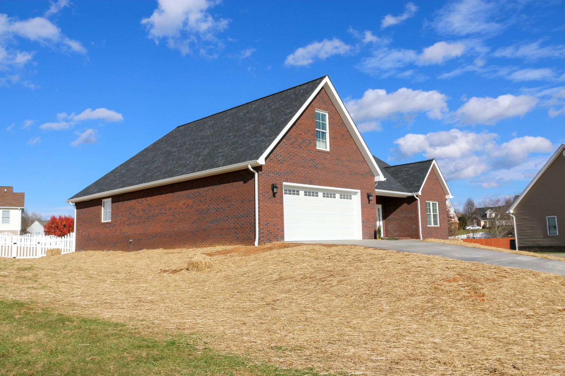 Brick suburban house with white garage door and steep roof on a grassy lot under a blue sky