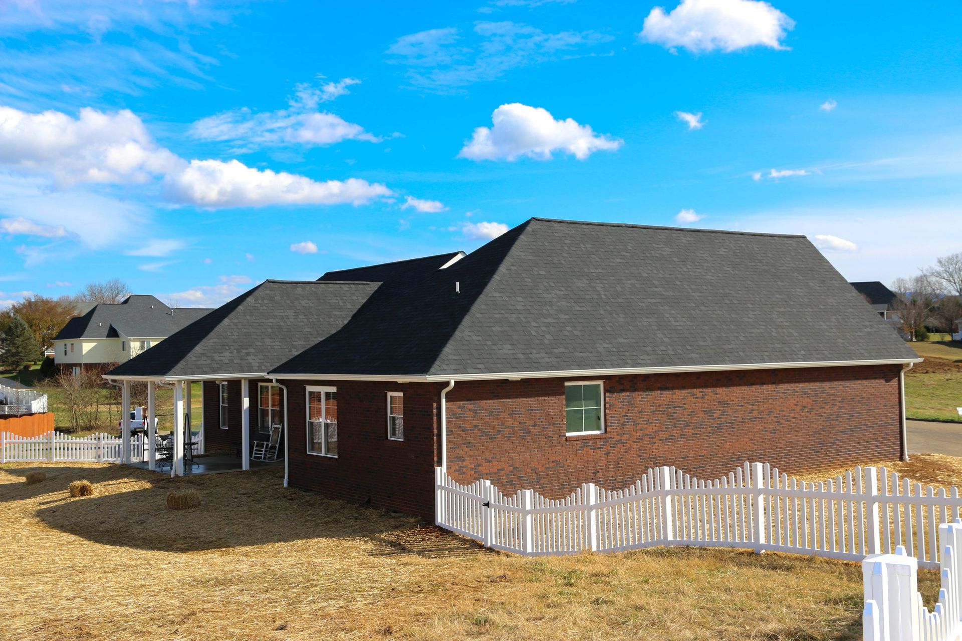 Single-story brick house with a dark roof and white picket fence under a blue sky.