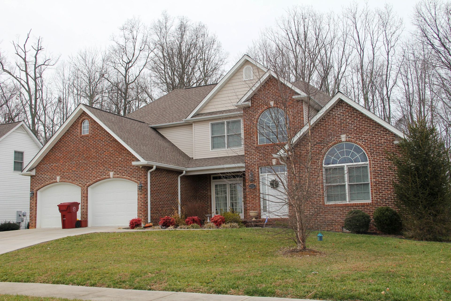 Brick suburban house with two-car garage, front lawn, and leafless trees in front