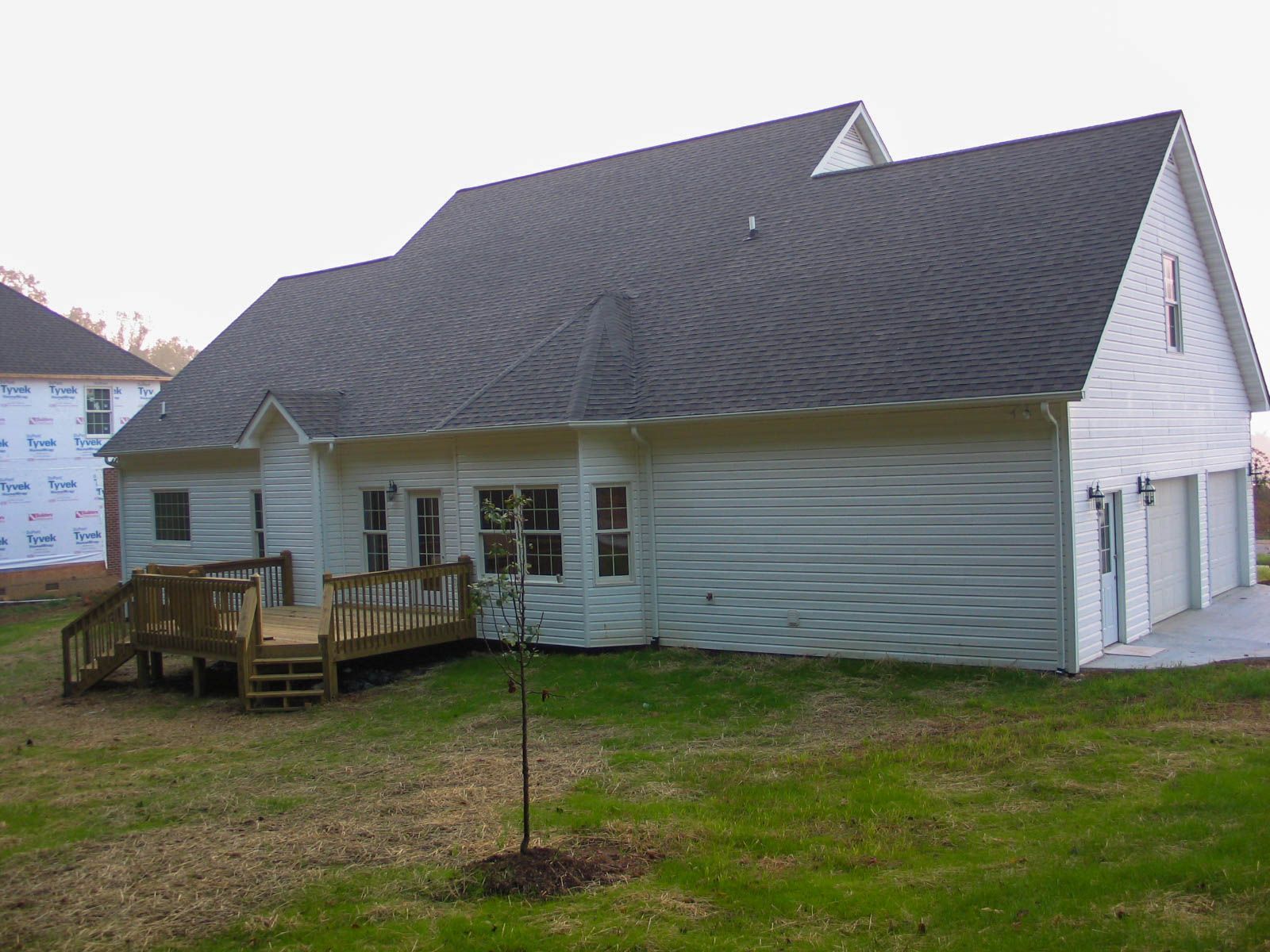 Suburban house with gray siding and roof, white trim, and a small wooden deck in a grassy yard.