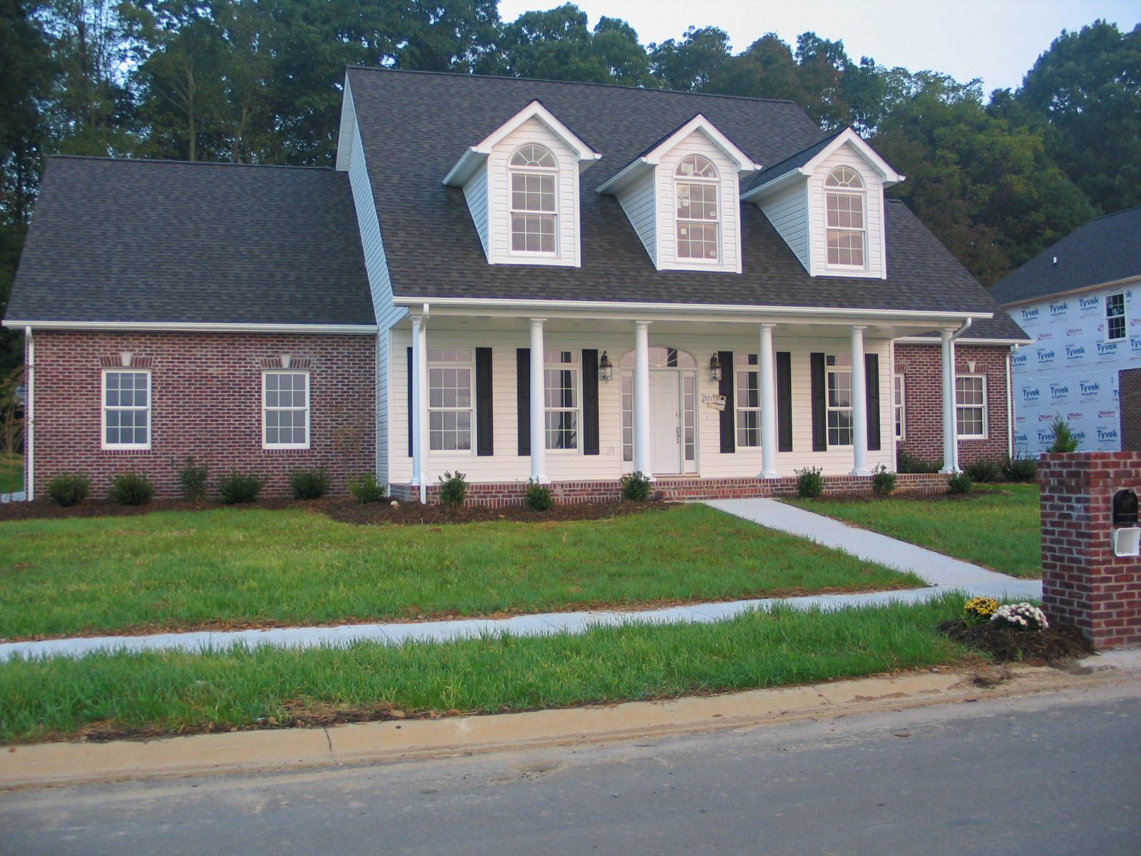 Suburban house with dark roof, white porch columns, brick and siding exterior, and a front lawn