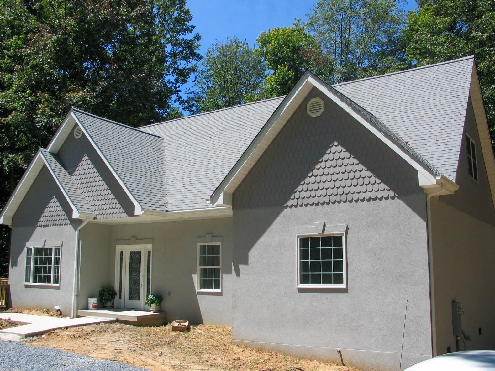 New gray house with gabled roof and white trim, viewed from the front yard under trees.