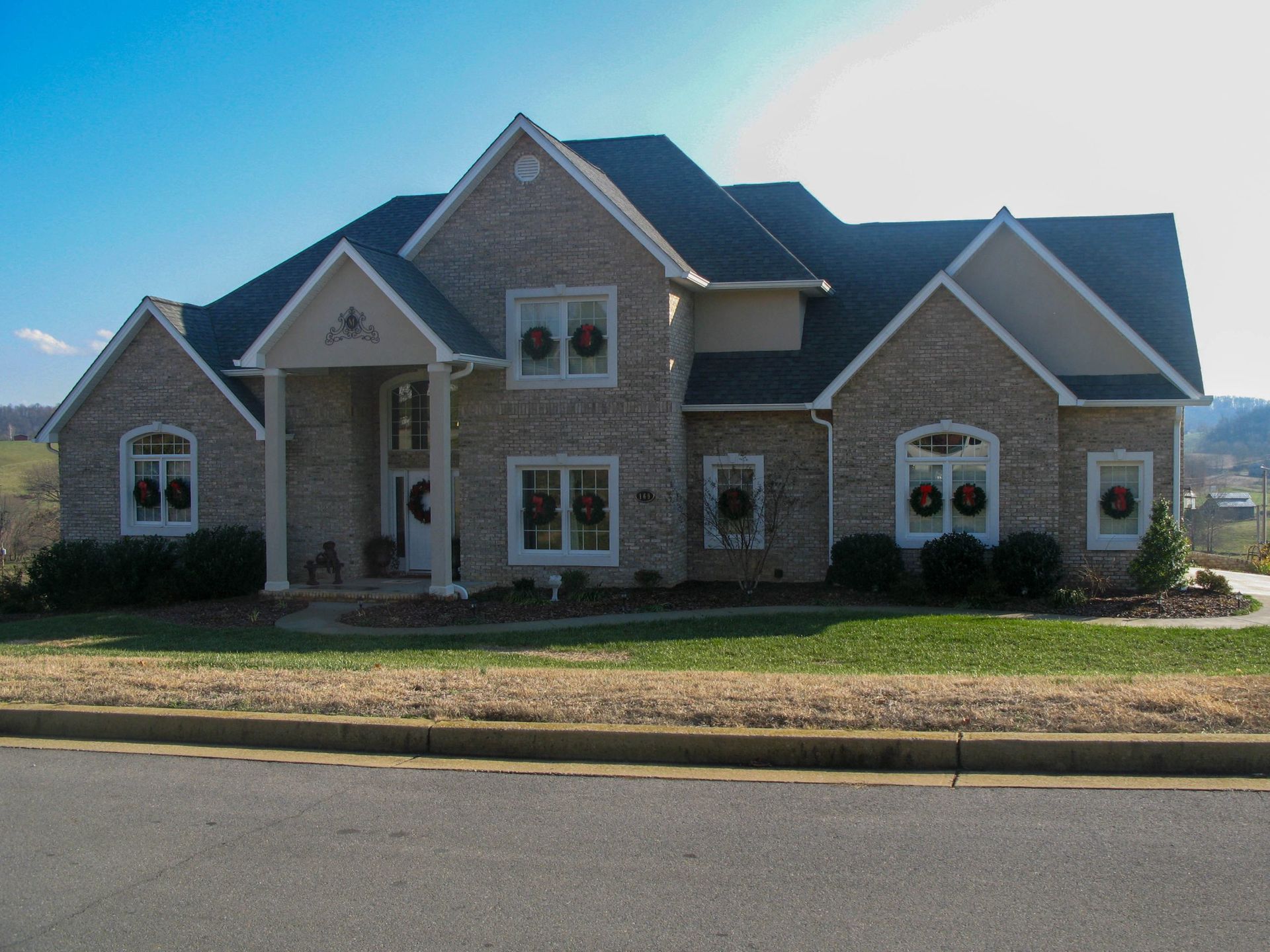 Large stone-and-brick suburban house with multiple gables and a front lawn under a blue sky