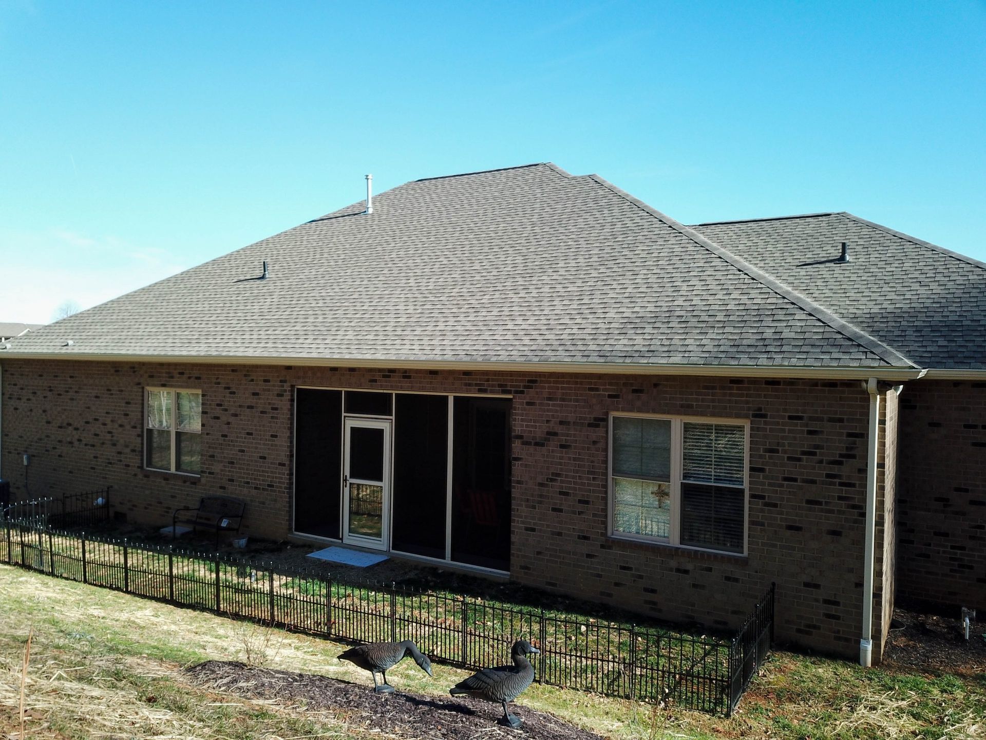 Brick house with a wavy shingle roof and front porch, viewed from the yard under a clear blue sky