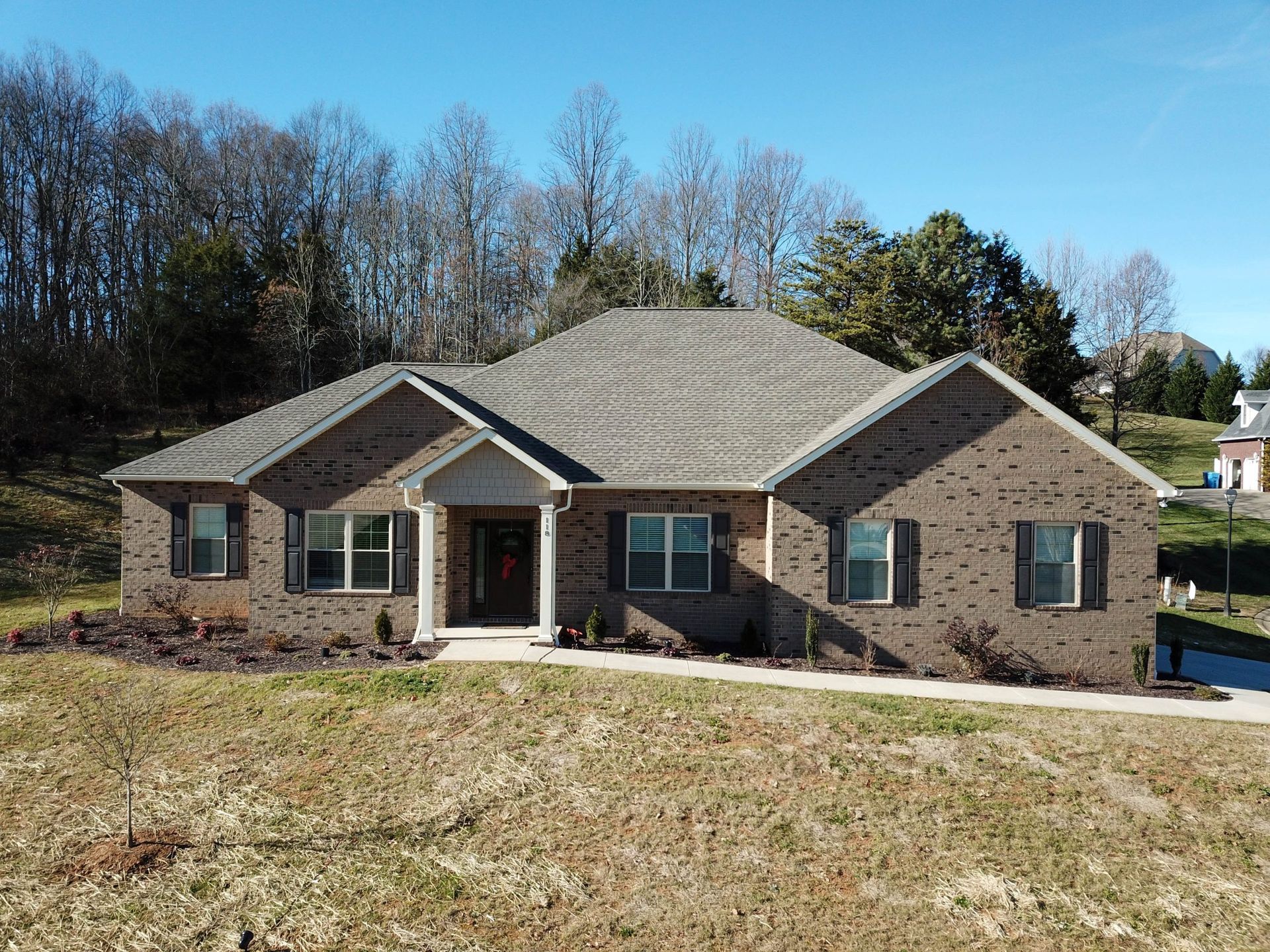 Single-story brick house with a gray roof and front porch on a grassy lot under a clear sky