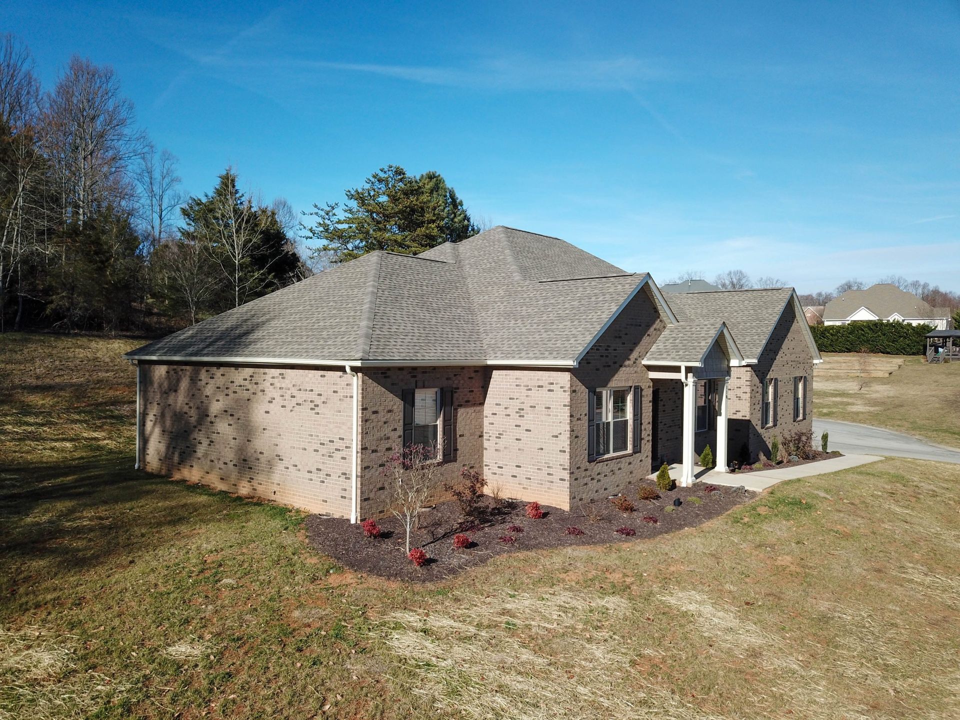 Single-story brick house with gray roof and small front porch on a grassy lot under a clear blue sky
