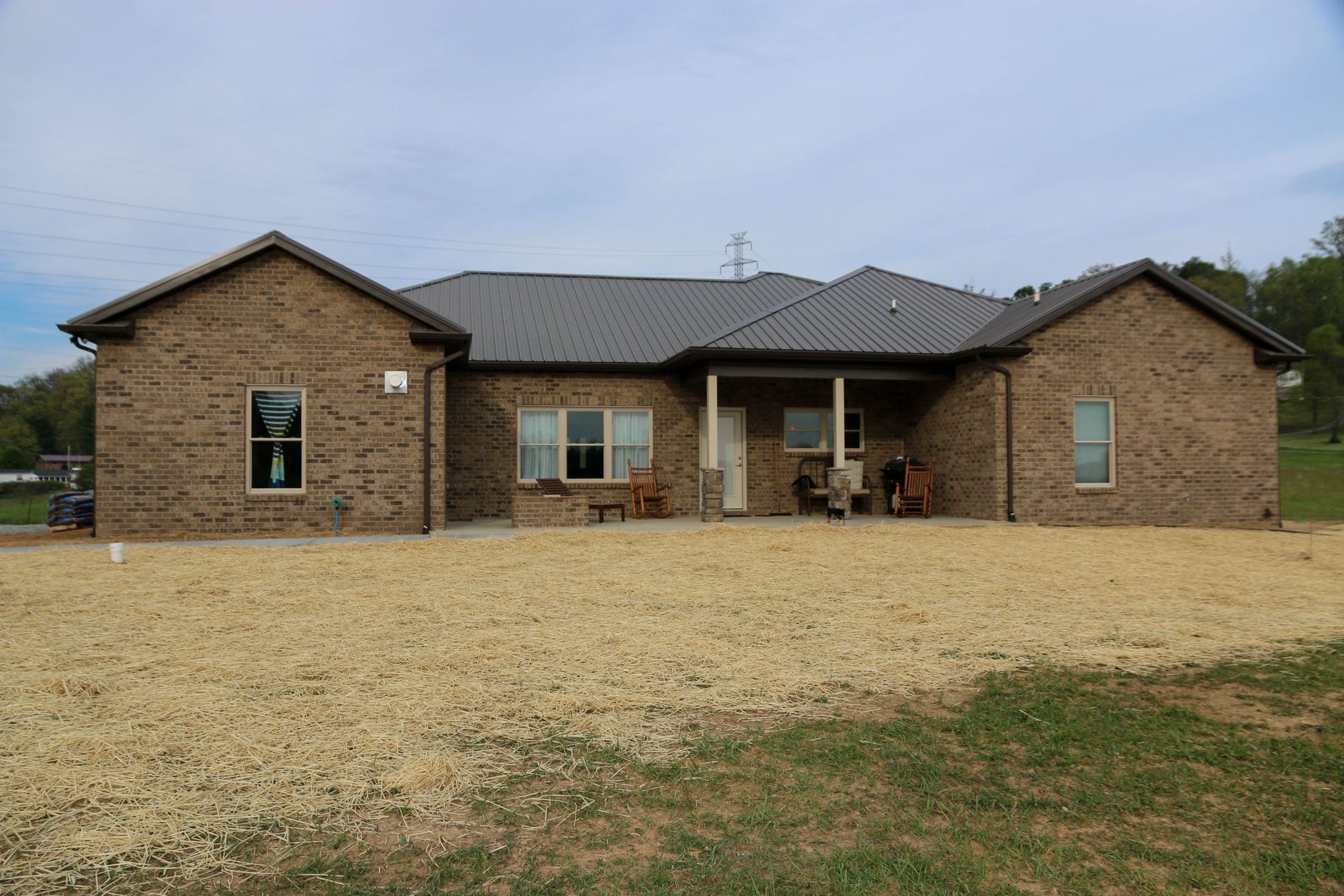 Single-story brick house with a dark roof and large gravel driveway under an overcast sky