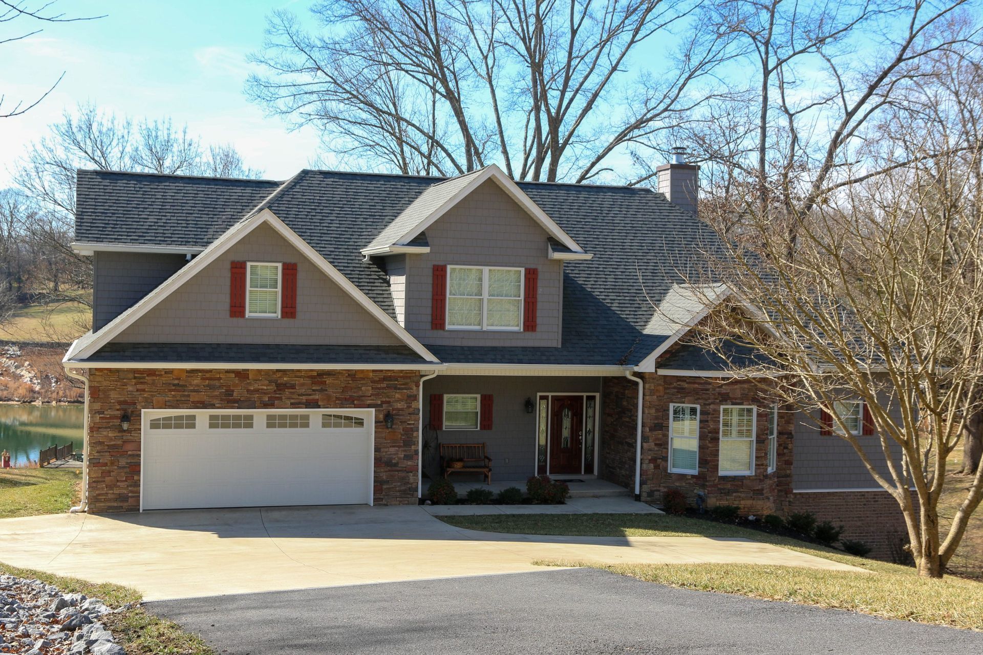 Suburban brick house with a two-car garage, gray roof, and red shutters on a sunny day