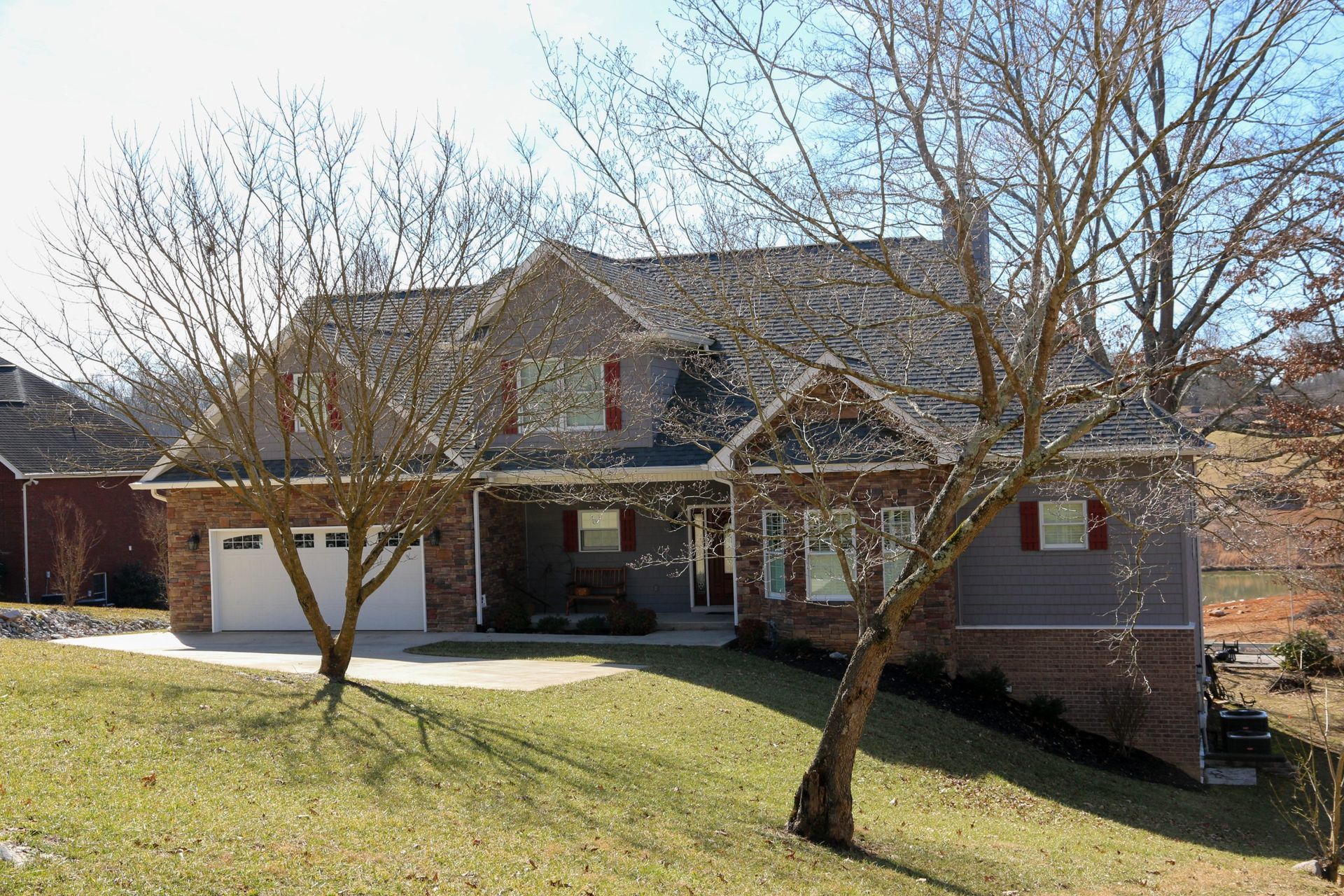 Suburban brick house with a front porch, garage, and leafless trees in winter sunlight