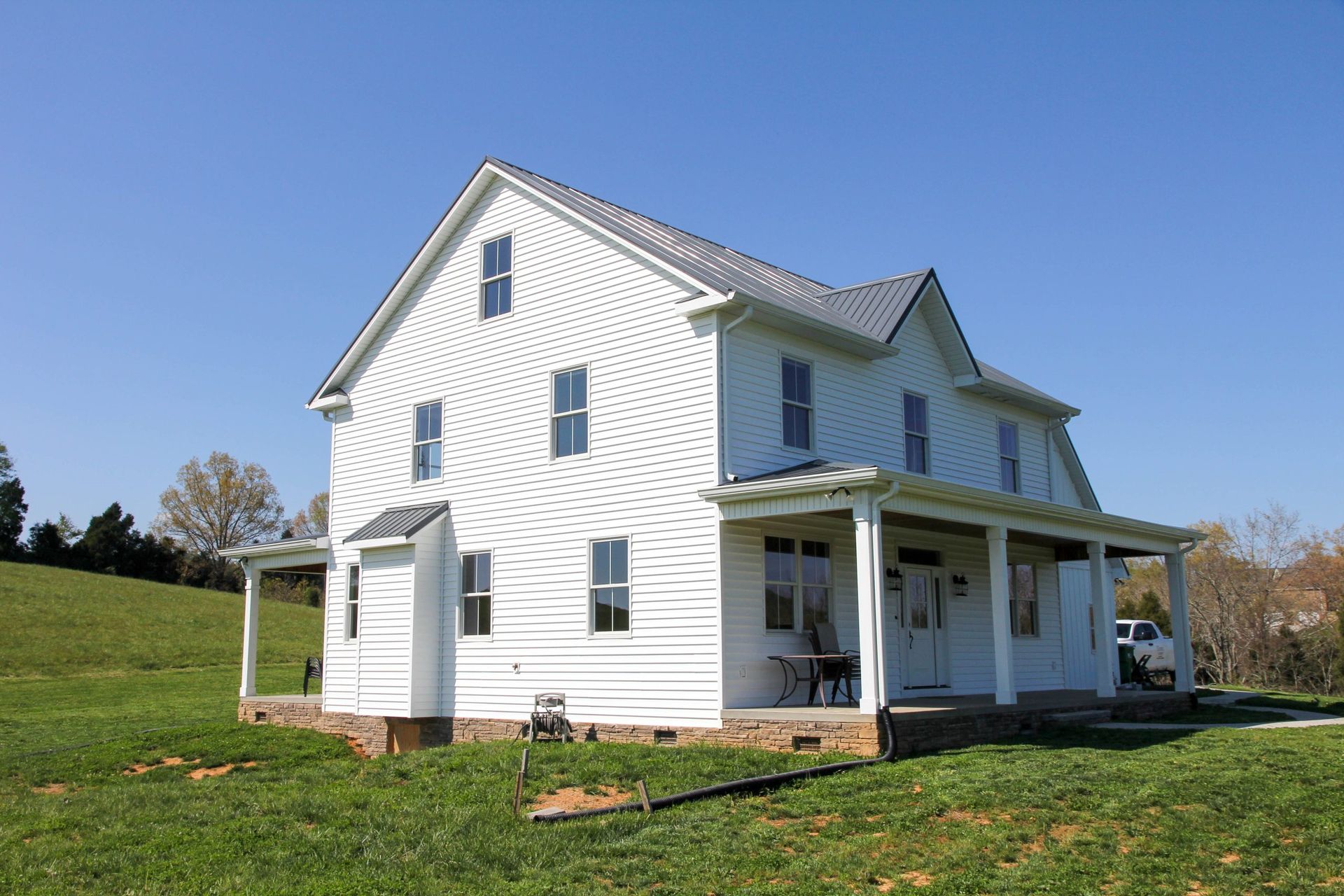 White two-story farmhouse with porch on a grassy hill under a clear blue sky