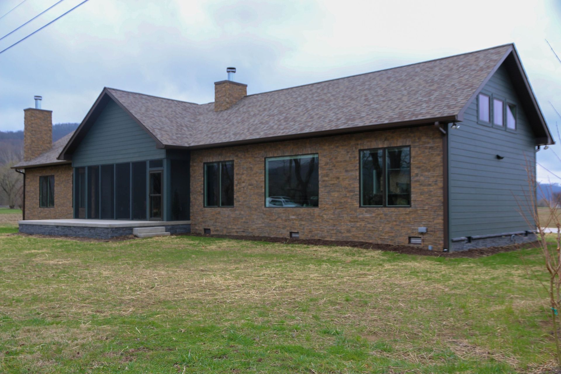 Single-story brick and gray house with a sloped roof and large yard under an overcast sky