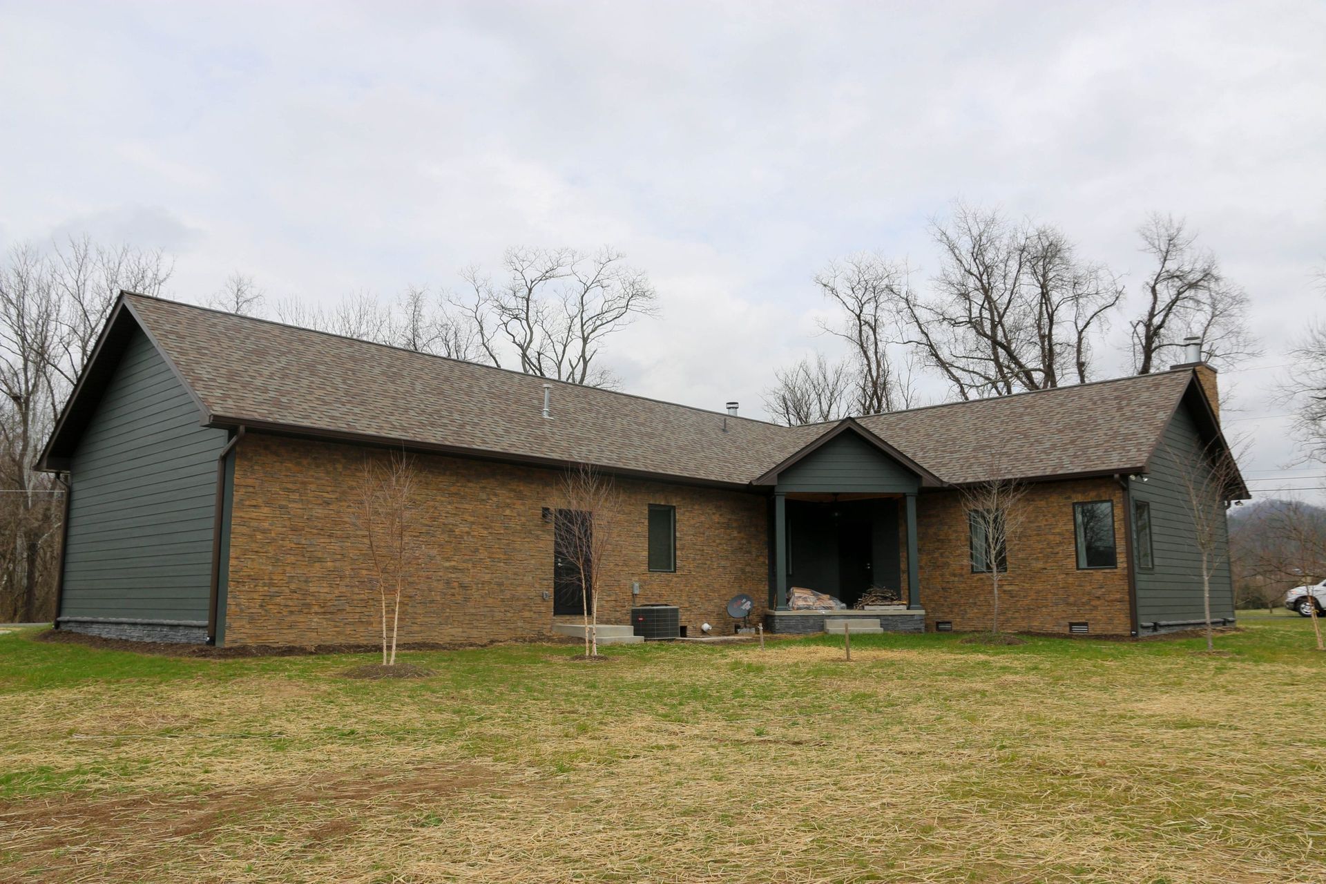 Single-story brick house with dark green siding and a front porch in a grassy yard
