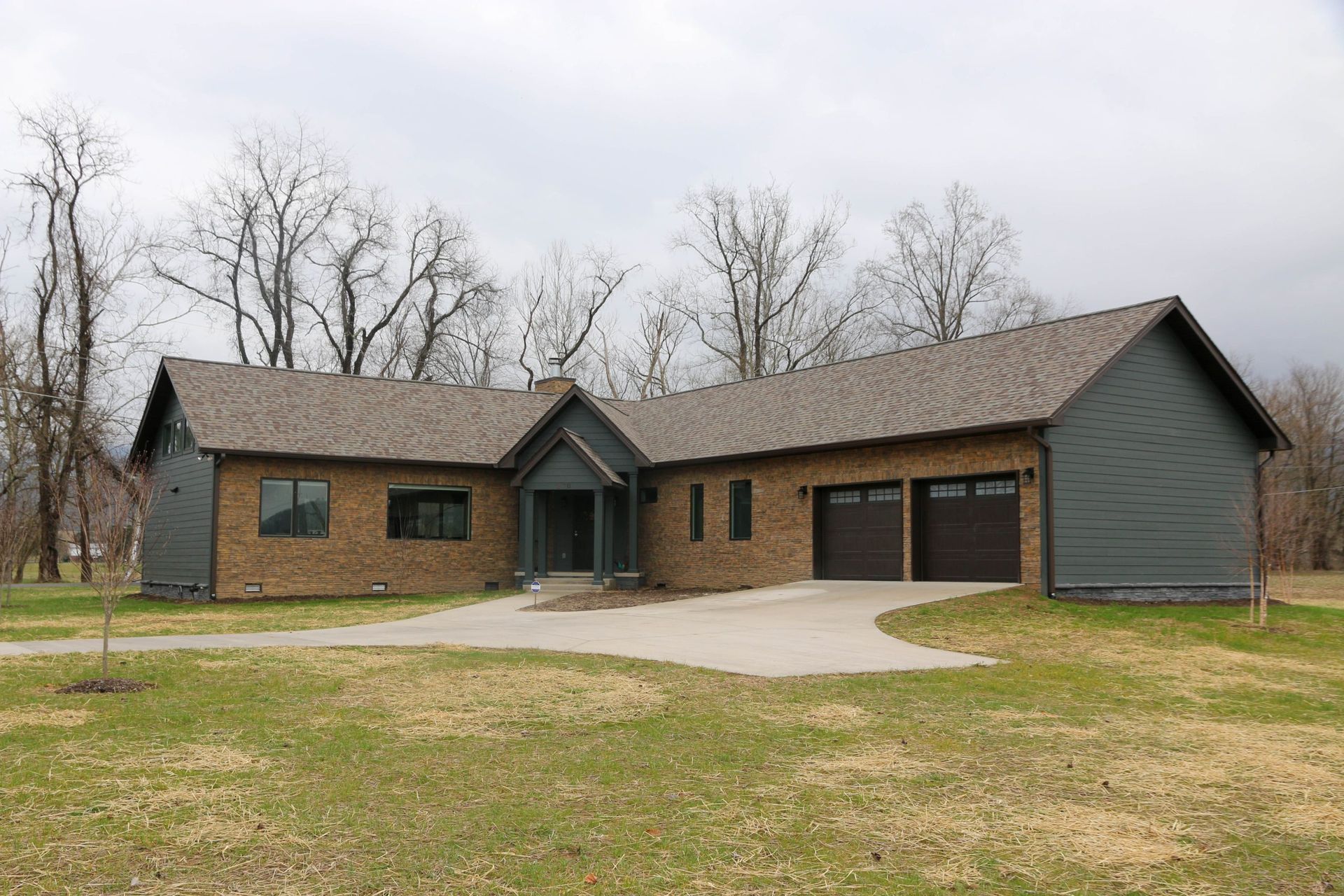 Single-story gray house with brown roof, garage, and front lawn under bare trees