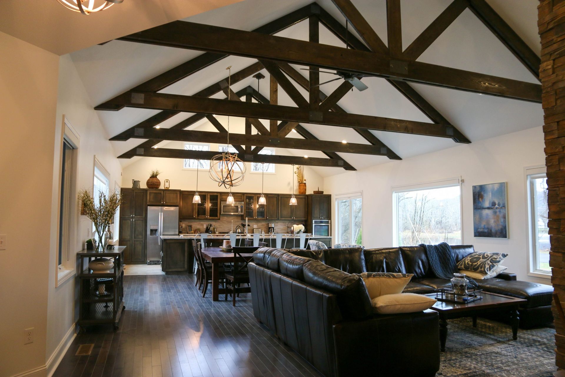 Modern open-plan living room with exposed wooden beams, leather sofas, and a kitchen in the background