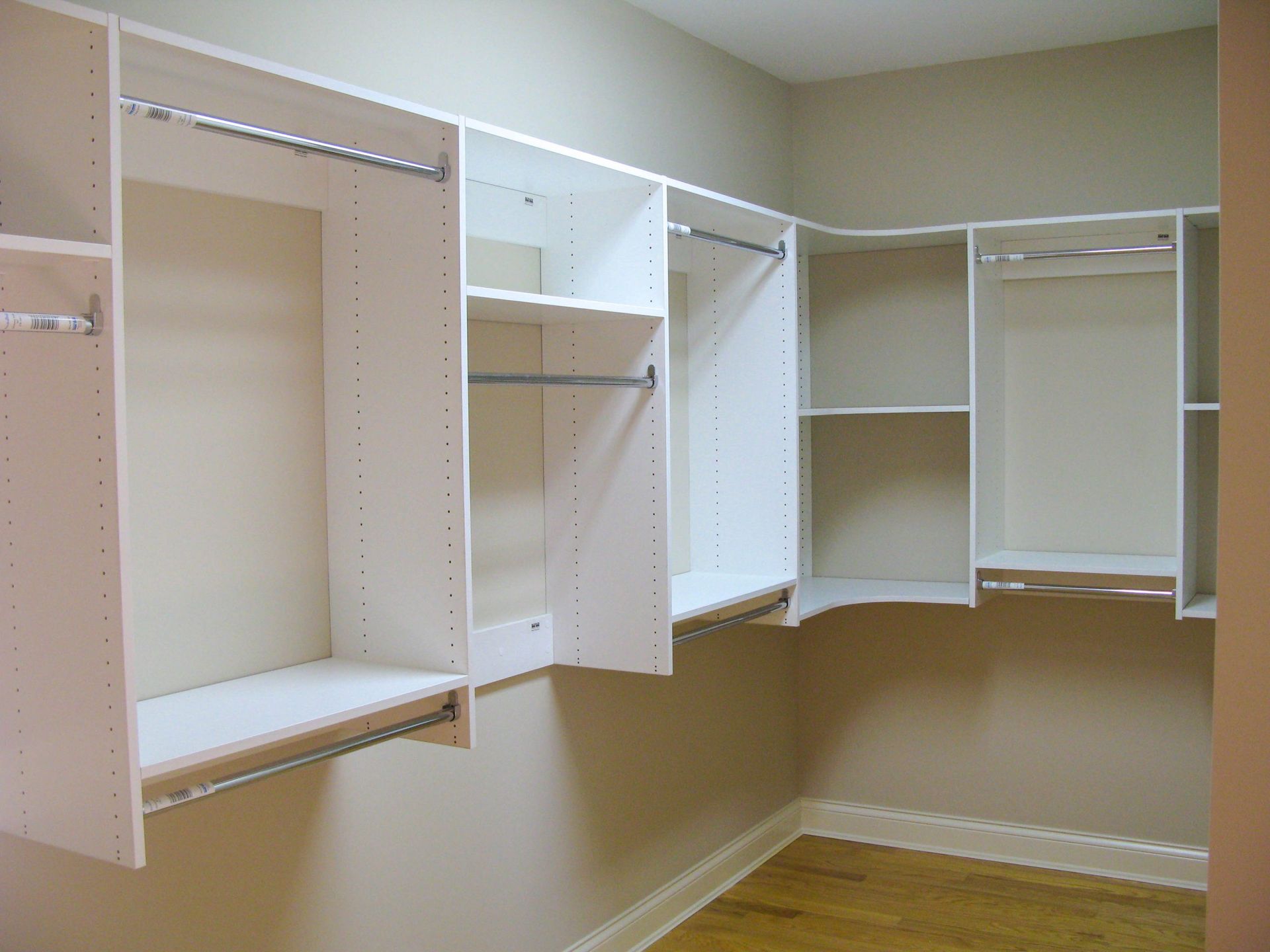 Empty beige walk-in closet with white built-in shelving and hanging rods